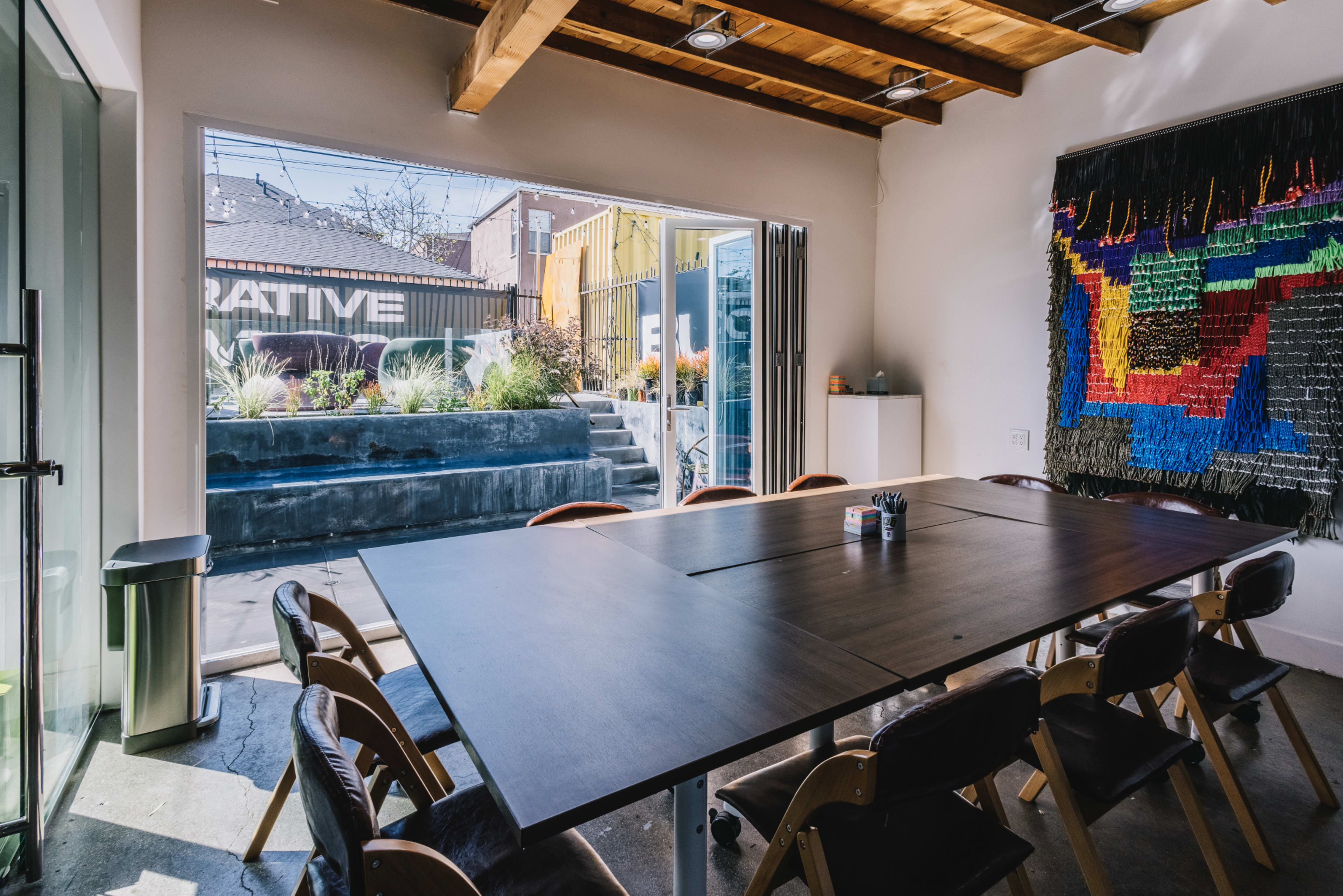 A spacious conference room features a large wooden table surrounded by chairs, with sliding glass doors opening to a landscaped outdoor area.