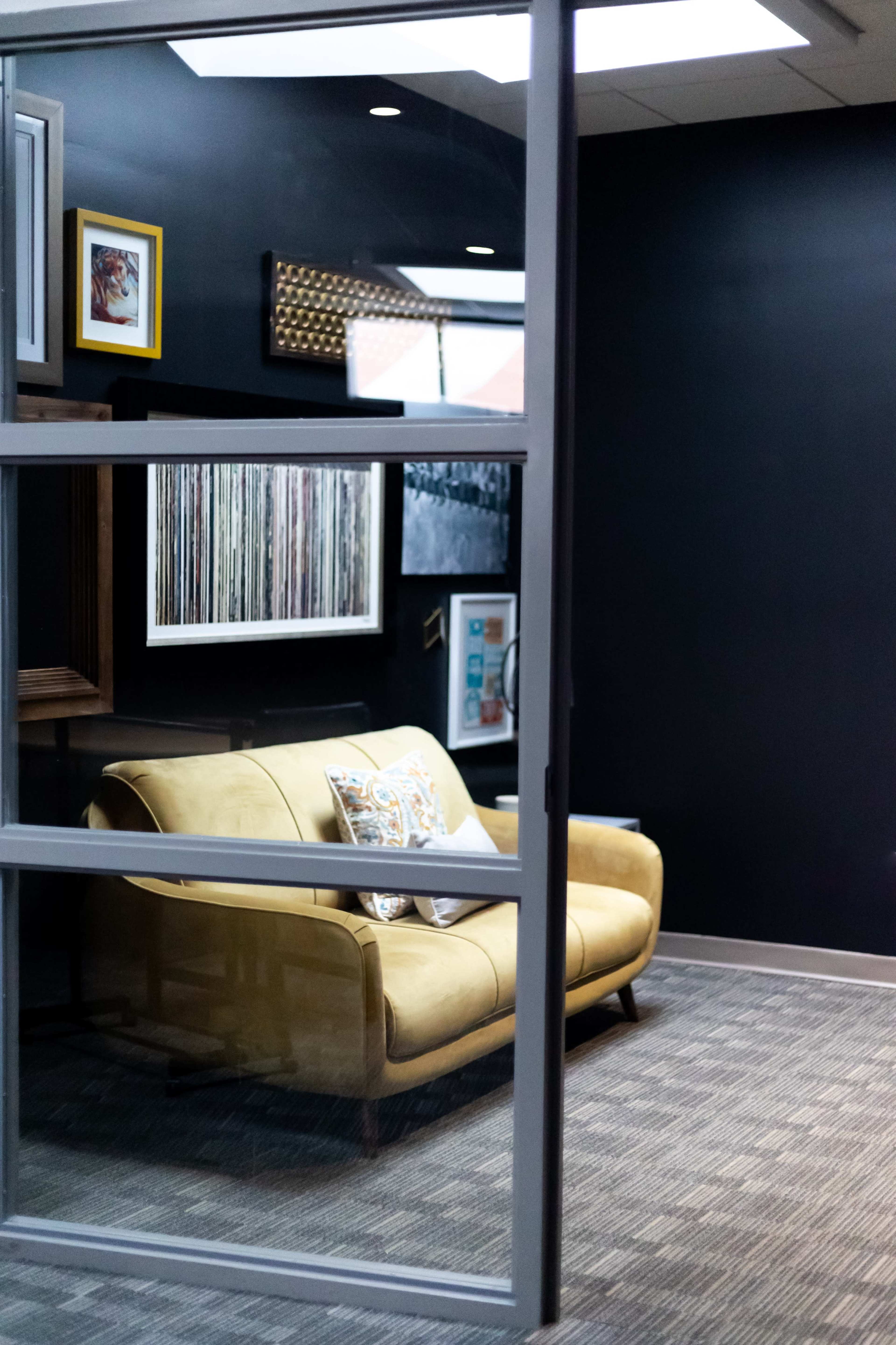 A cozy yellow sofa in a modern office space, positioned near a wall with framed artwork.