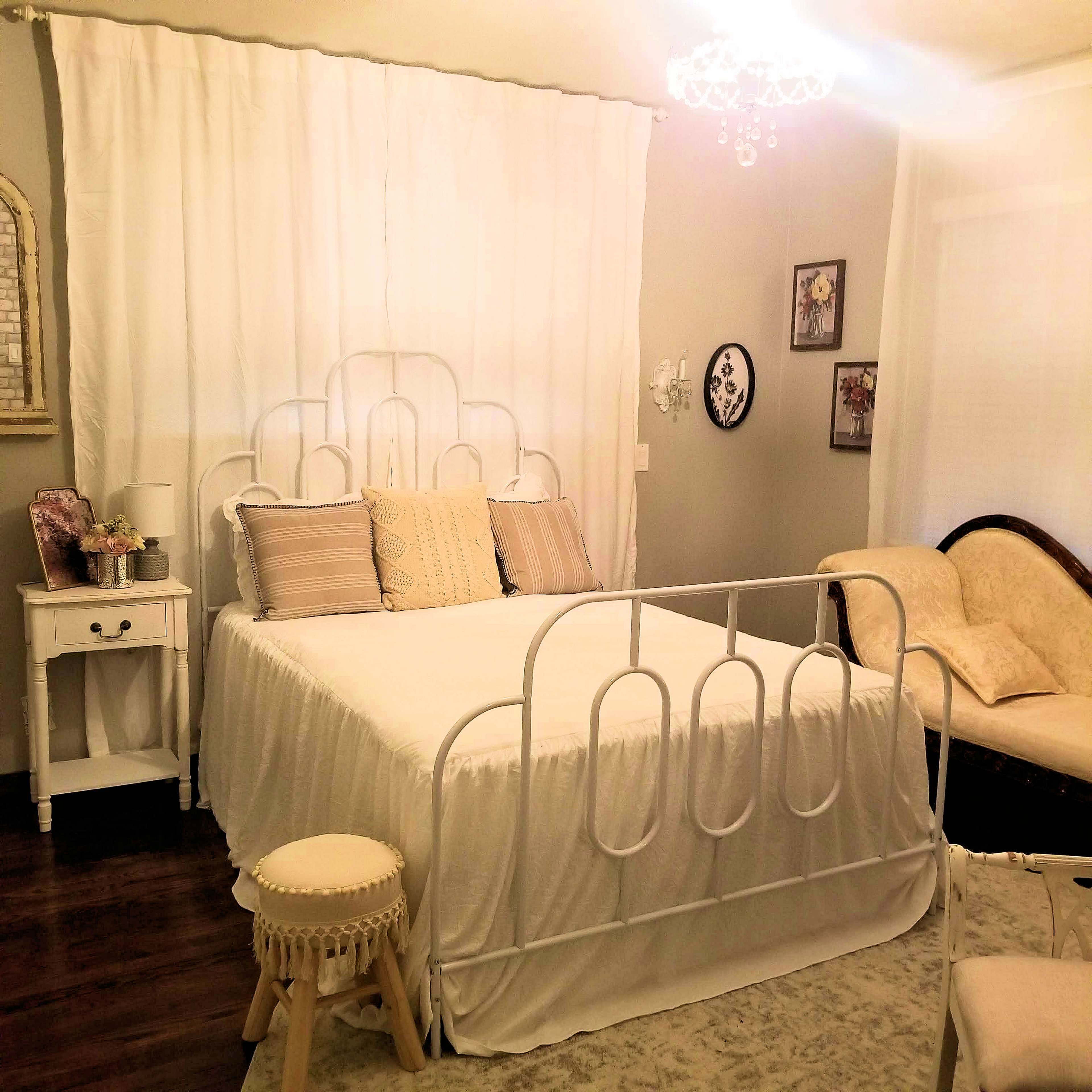 A cozy bedroom featuring a metal bed with a white bedspread, surrounded by light-colored walls and soft decorative elements.