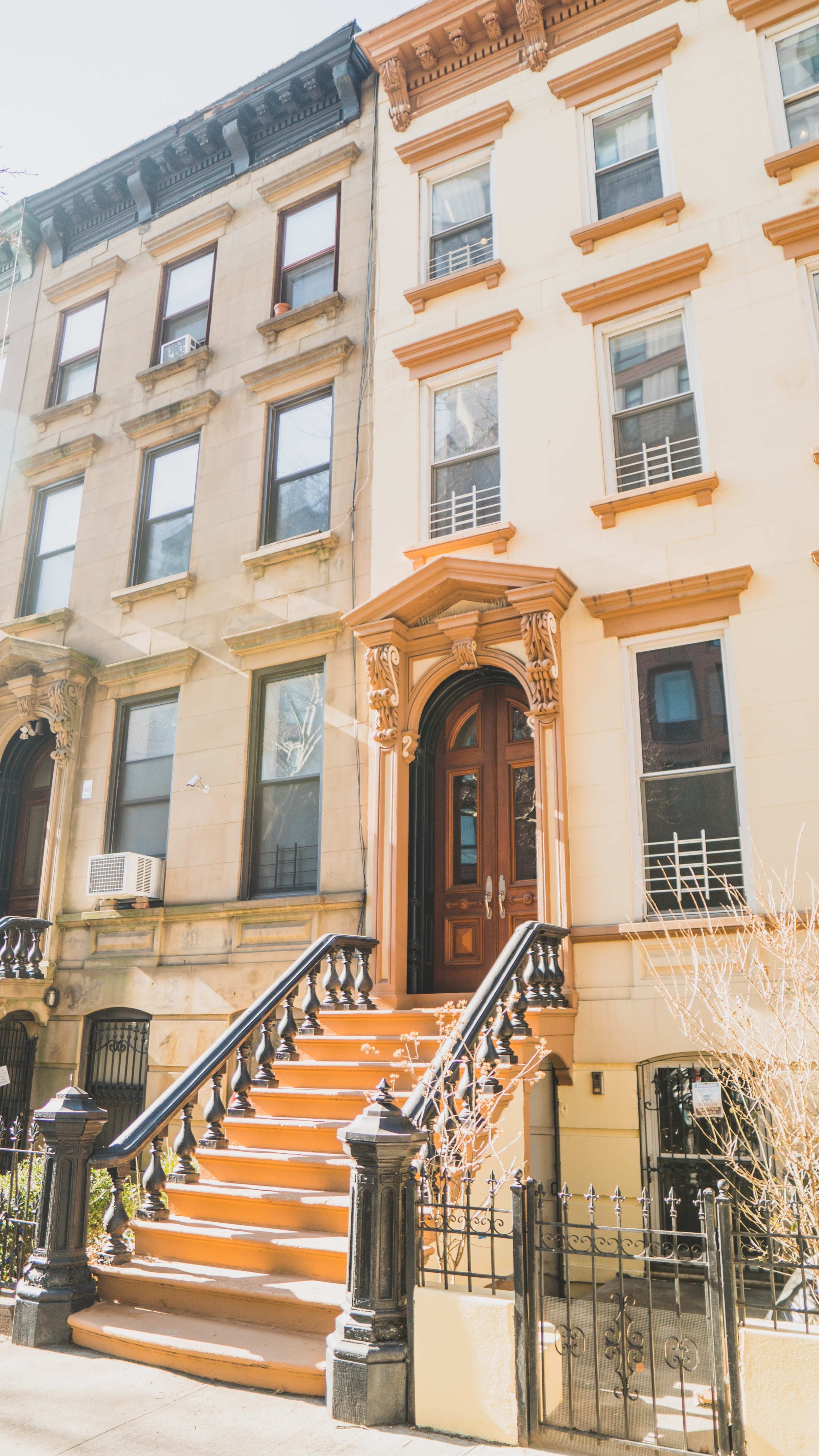The image shows a row of brownstone buildings with ornate entrances and well-defined steps leading to the front doors.