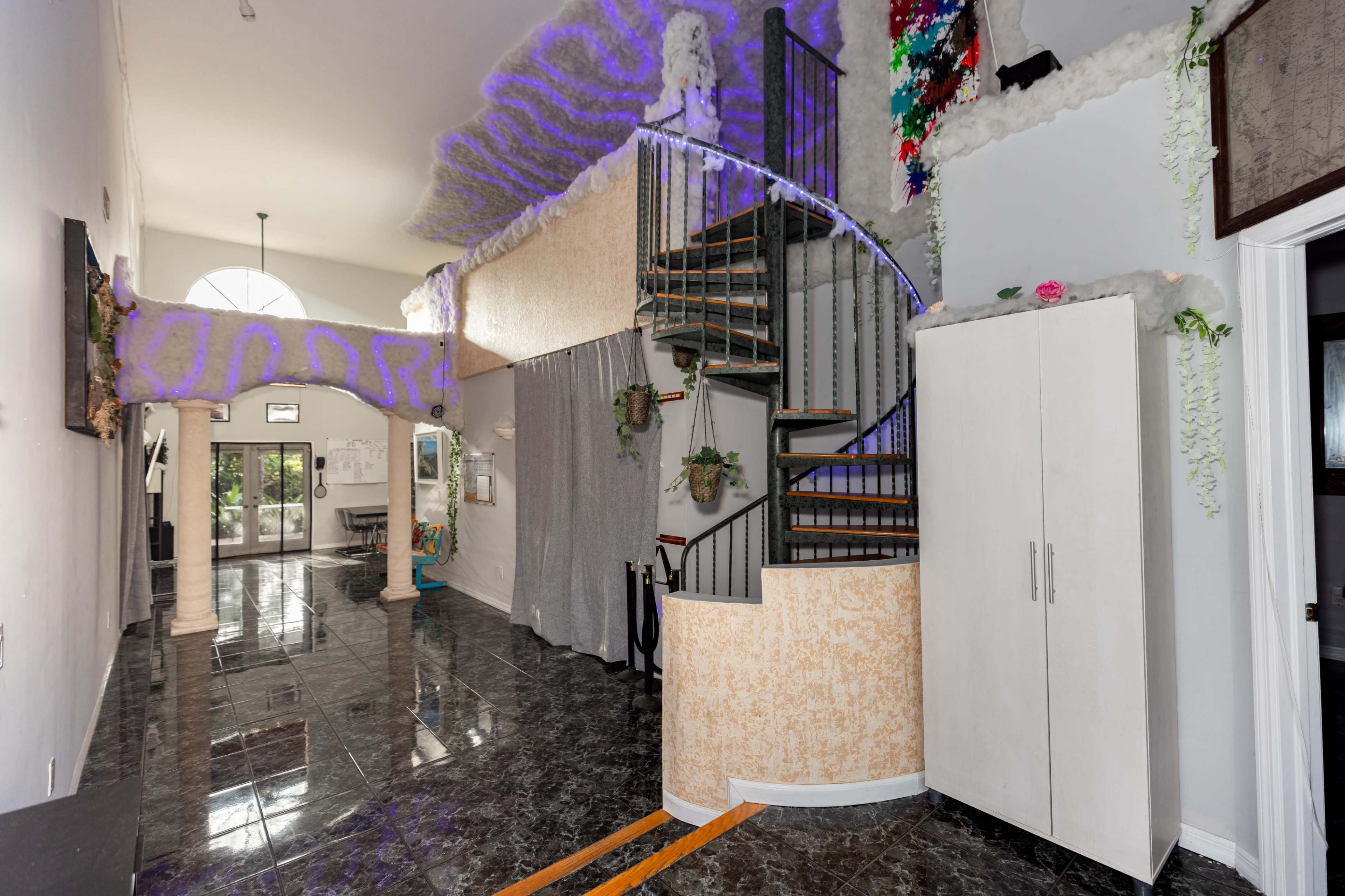 The image shows a spacious entryway with a spiral staircase, glossy dark floors, and decorative elements along the walls.