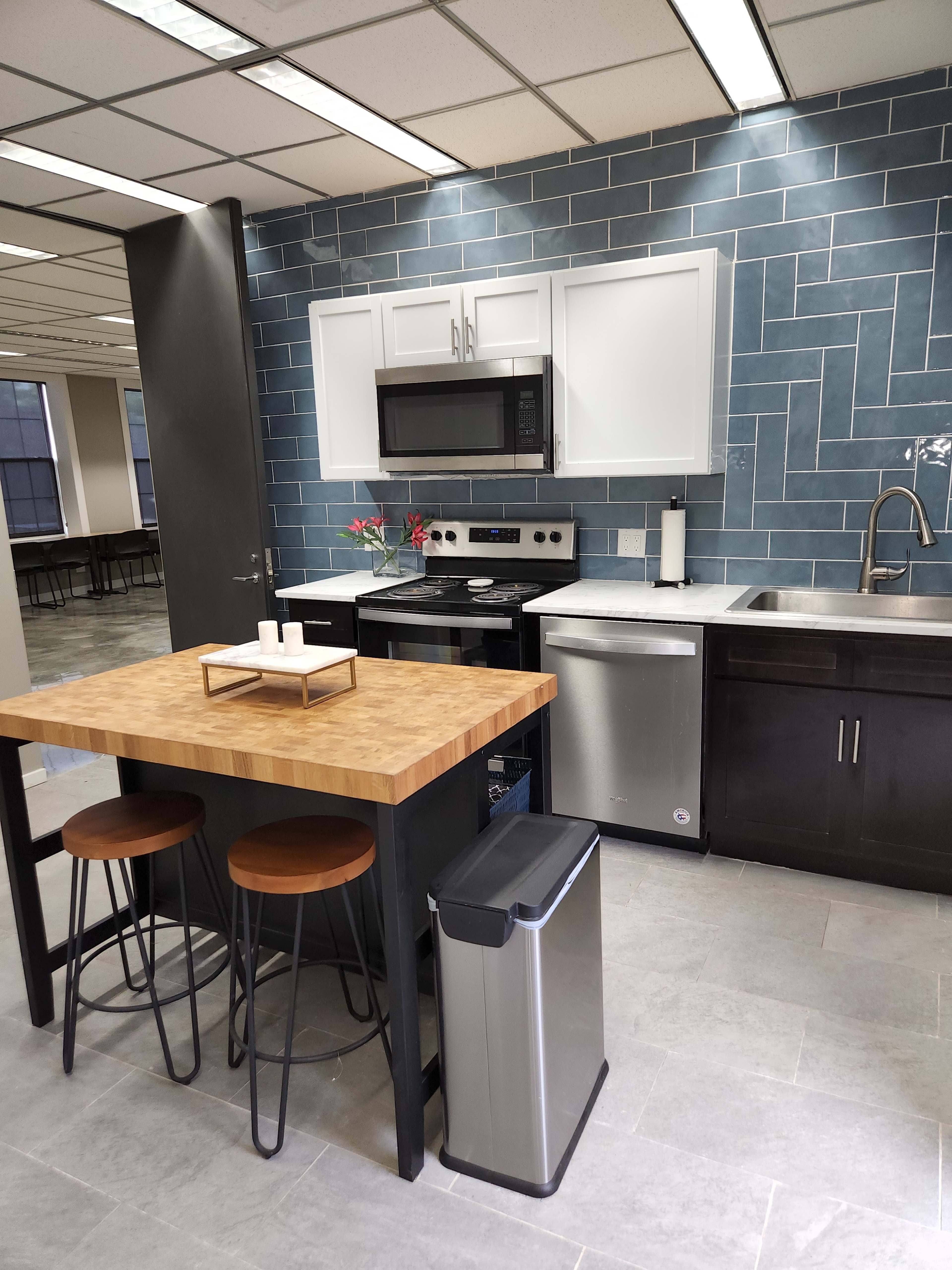 The image shows a modern kitchen featuring a black island with two bar stools, stainless steel appliances, and a blue tiled backsplash.