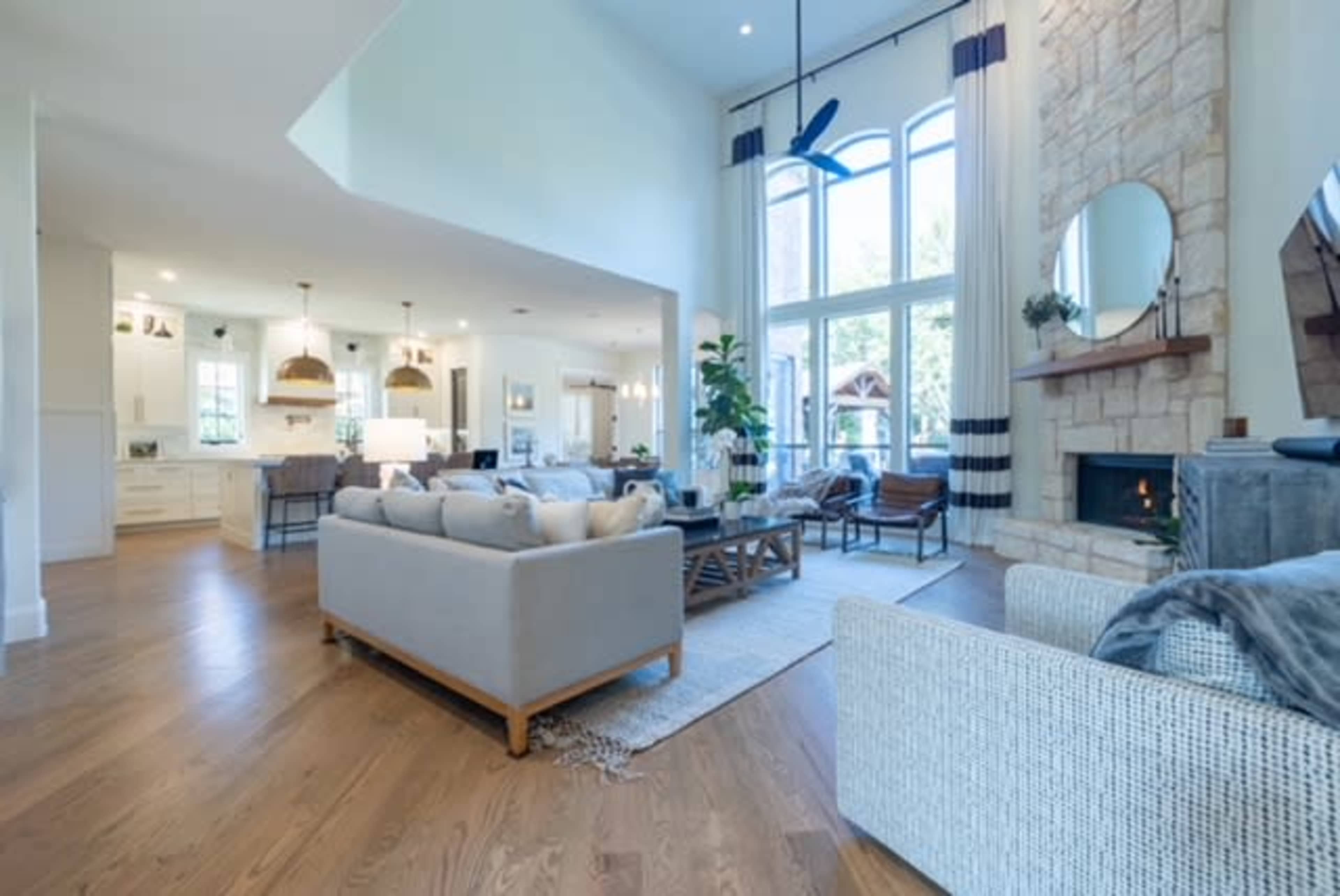 A spacious living area featuring large windows, natural wood flooring, and a mix of comfortable furniture arranged around a central coffee table.