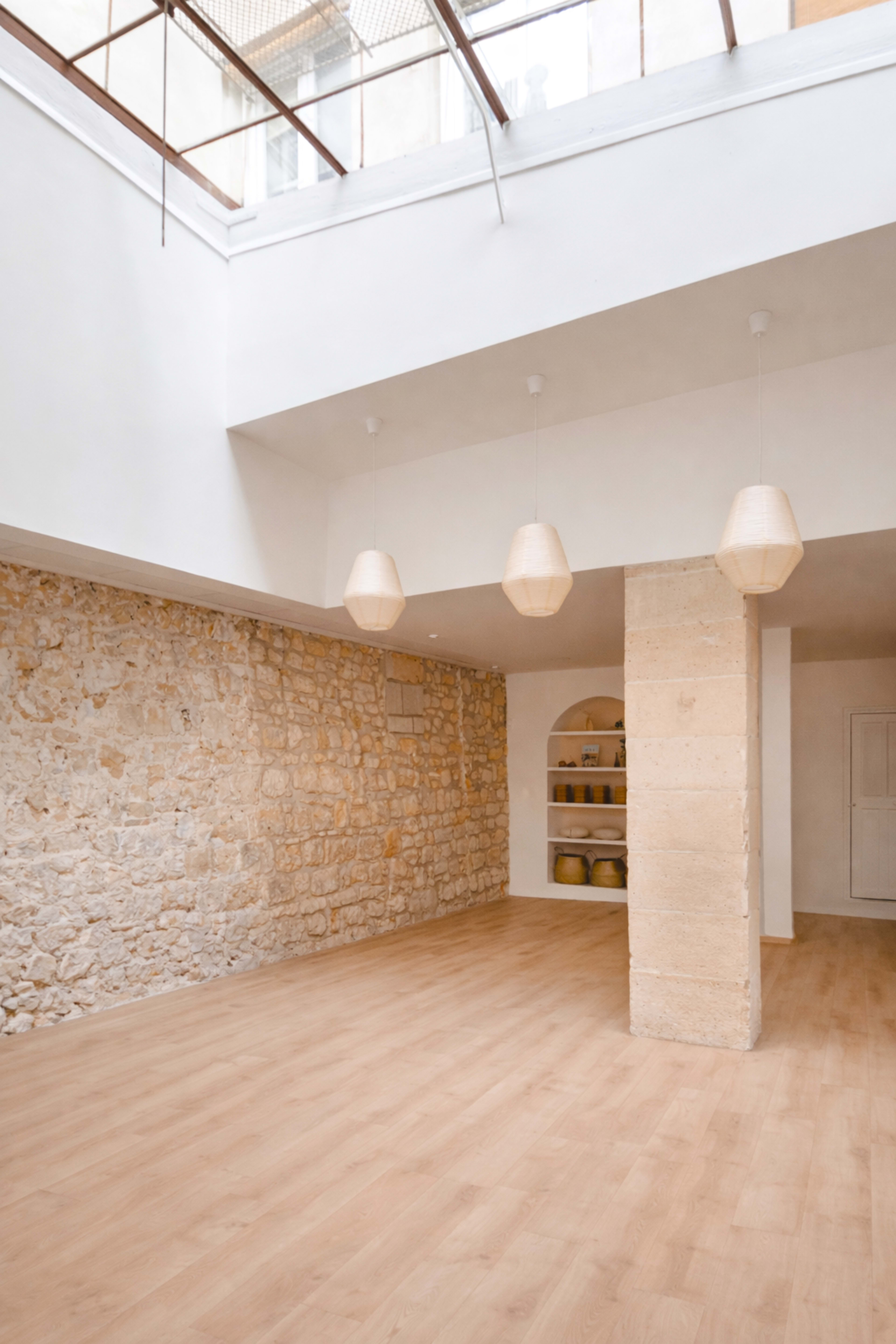 The image depicts a spacious interior with a stone wall, wooden flooring, and three pendant light fixtures hanging from the ceiling.