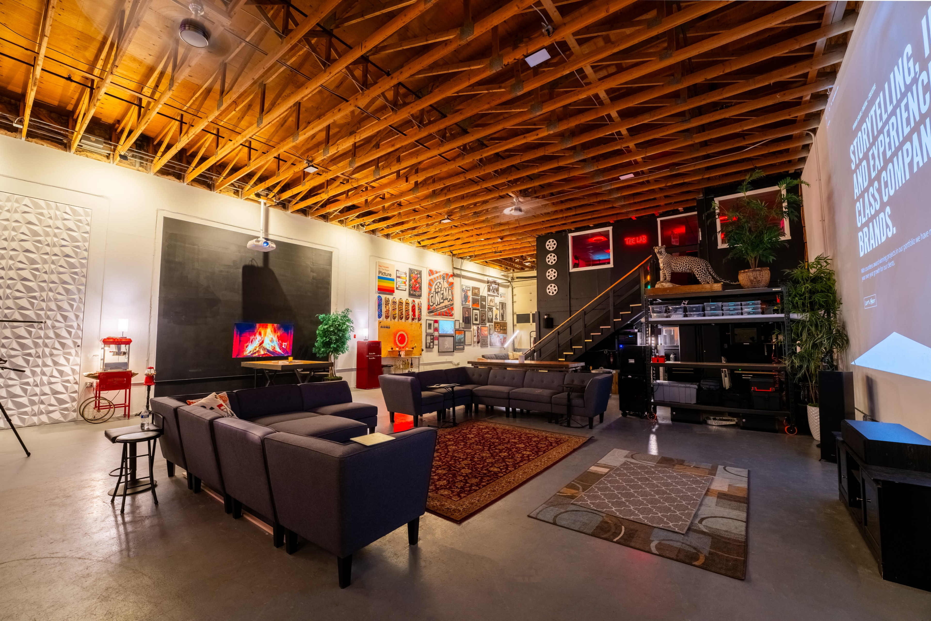 A spacious living room with a high wooden ceiling, modern furniture, and a large wall displaying a projector screen.