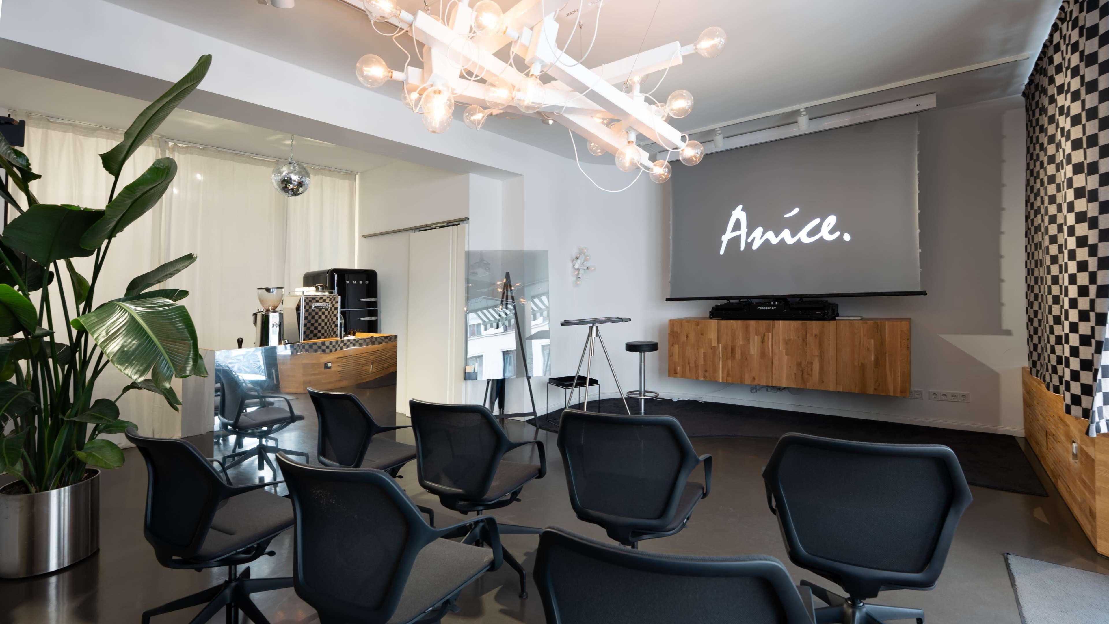 The image shows a modern event space with a projector screen displaying the word "Anice," surrounded by black chairs and contemporary decor.