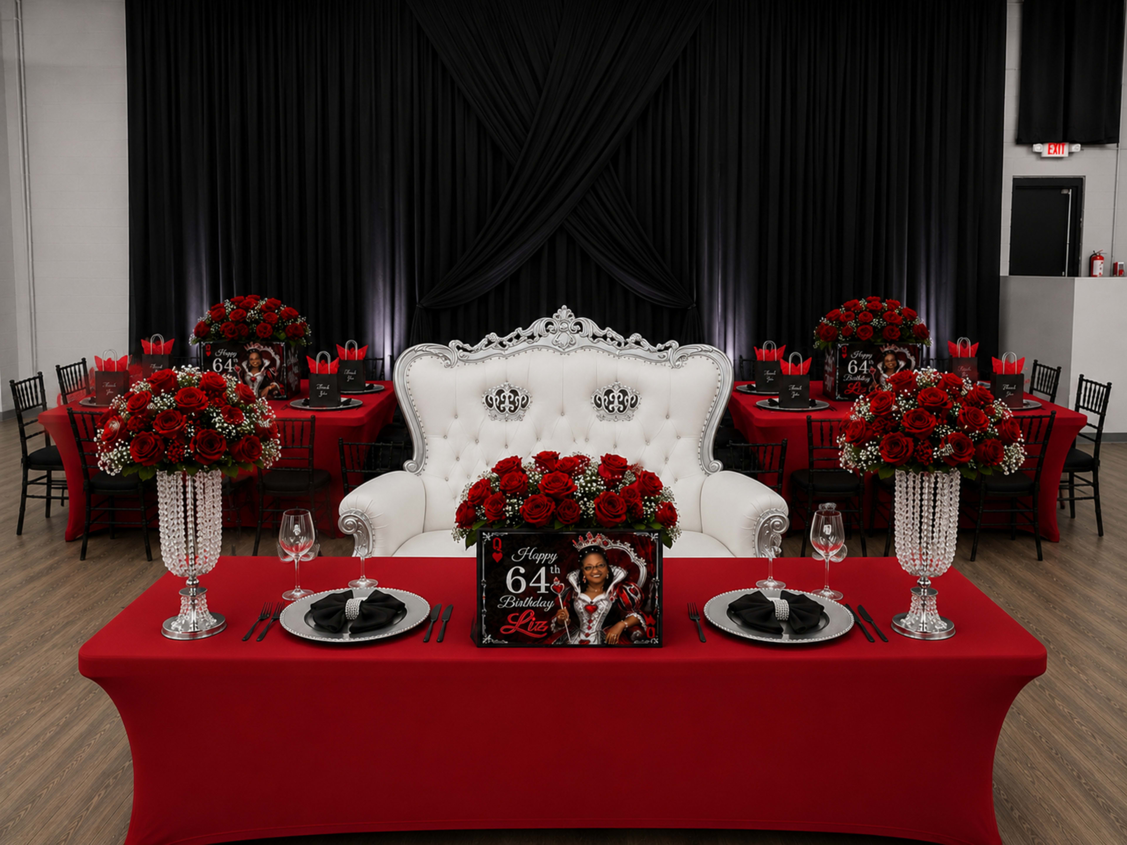 The image depicts a banquet setup featuring a lavish white throne chair, red tablecloths, and ornate floral arrangements centered on each table.