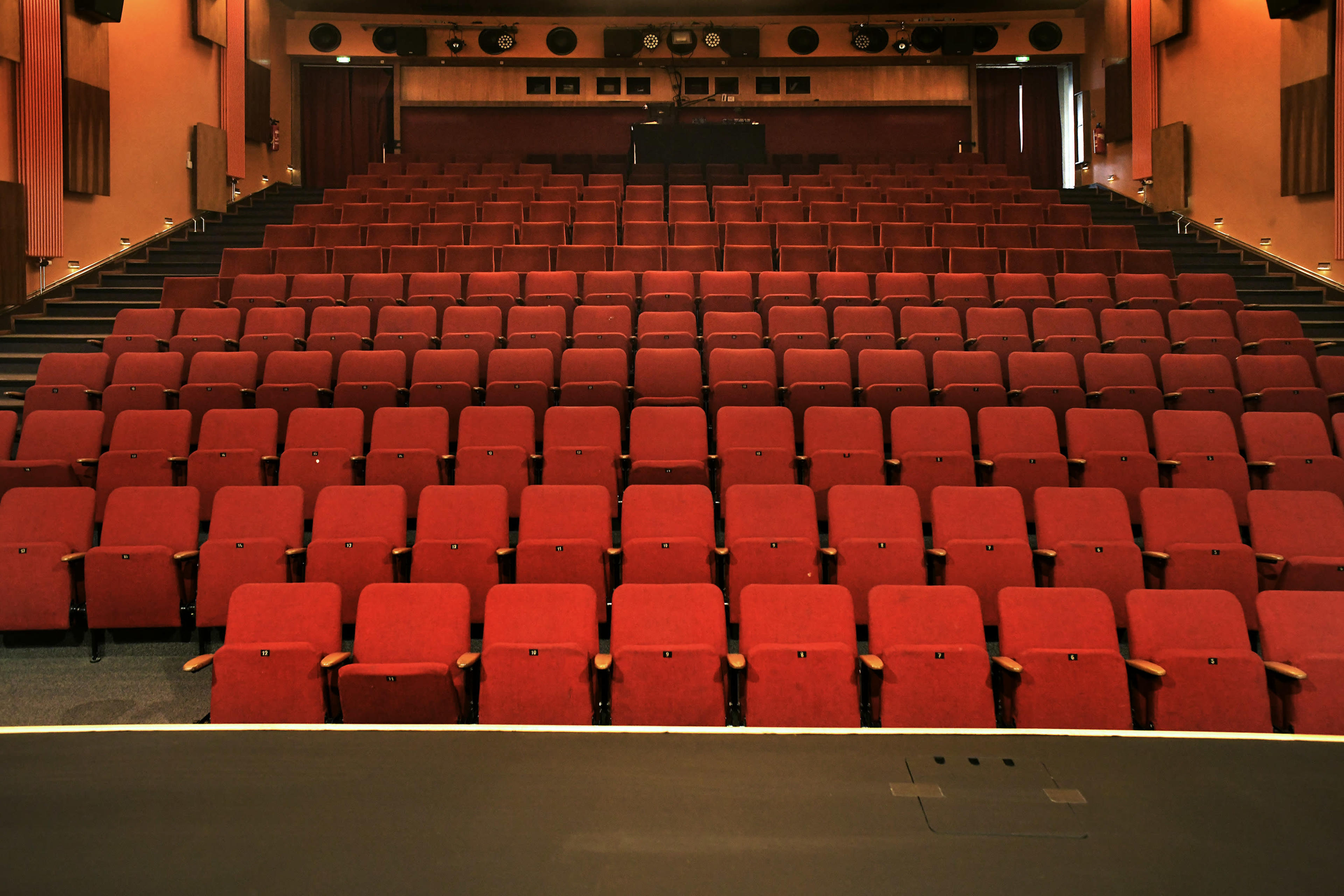The image shows a theater auditorium with rows of red upholstered seats arranged in a tiered formation.
