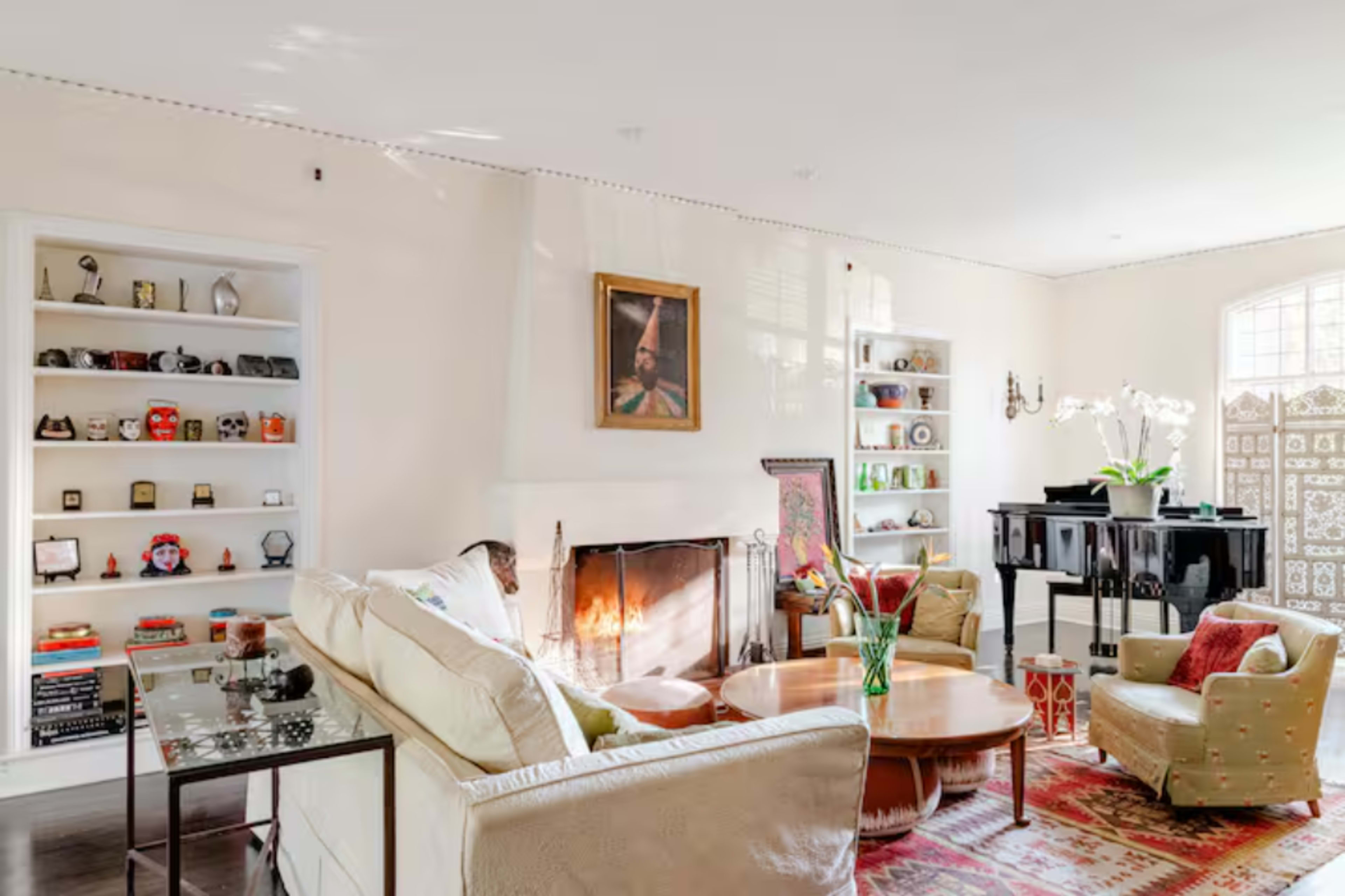 A well-lit living room features a cozy seating area, a fireplace, and shelves displaying various decorative items.