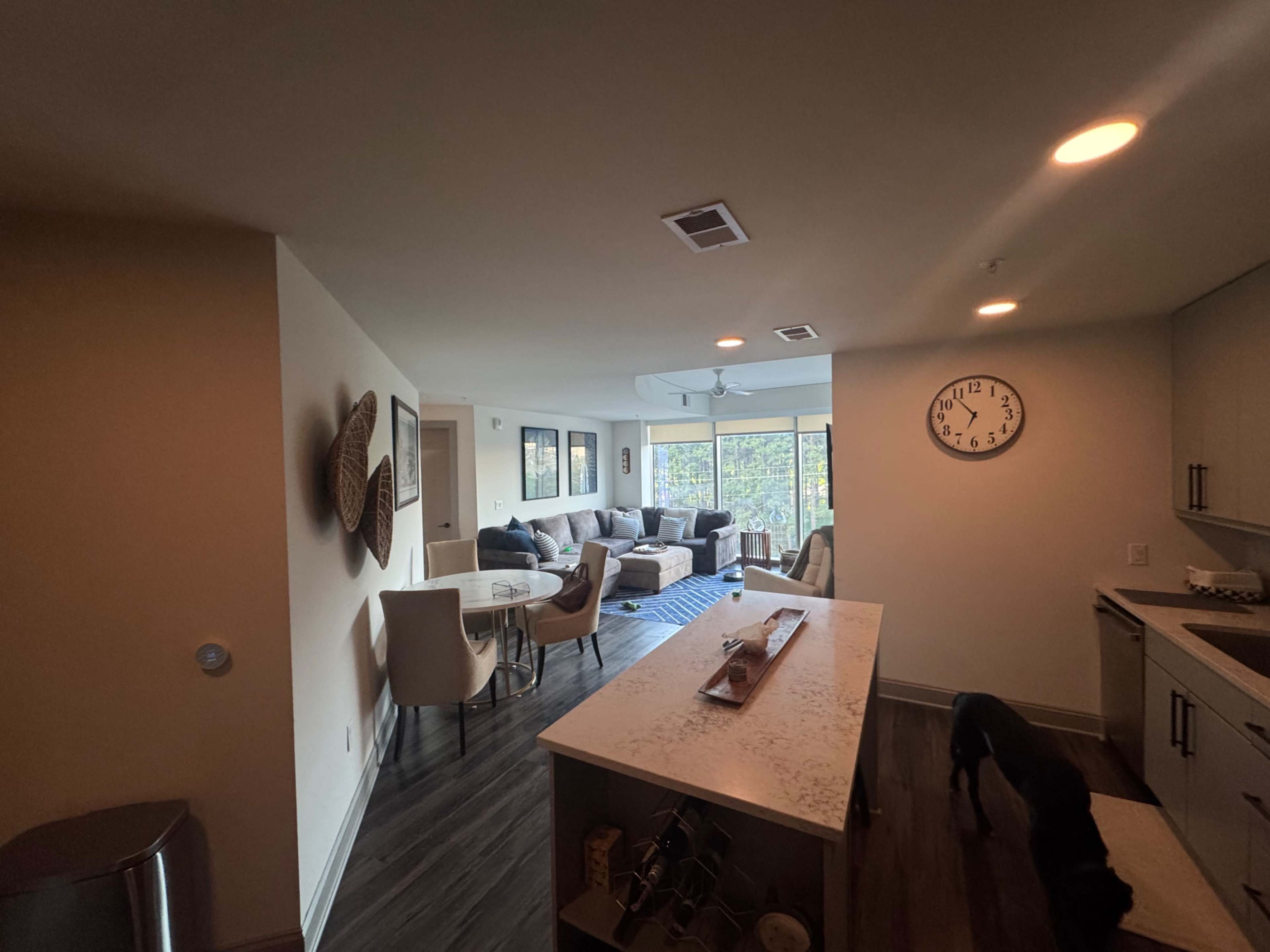 The image shows a modern open-concept living space with a kitchen island, dining area, and a living room featuring a large window.