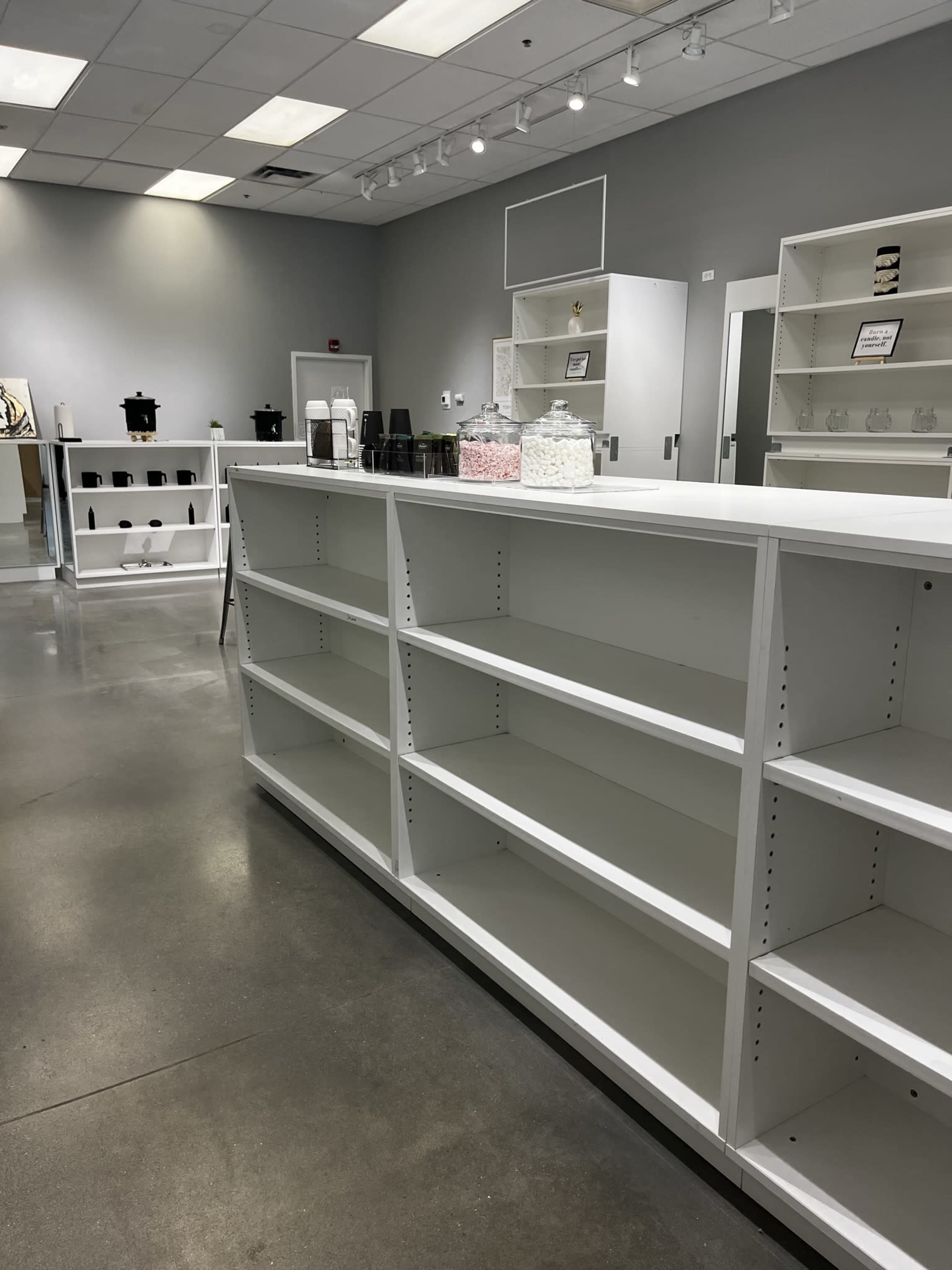 A spacious, vacant retail space with white shelving units and minimal decor.