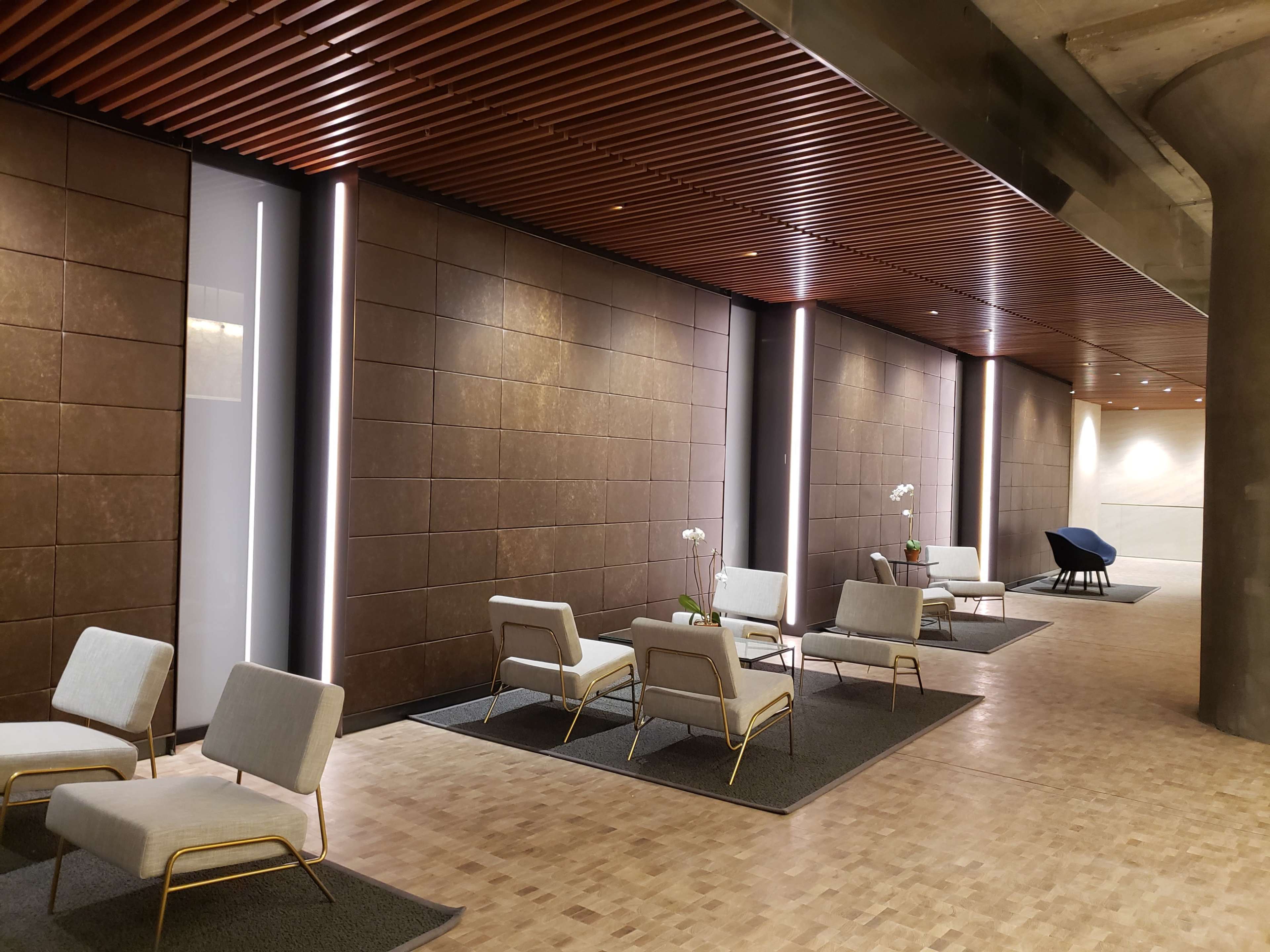 The image shows a modern interior space featuring minimalist seating arrangements with chairs and tables, illuminated by vertical light strips along the walls.