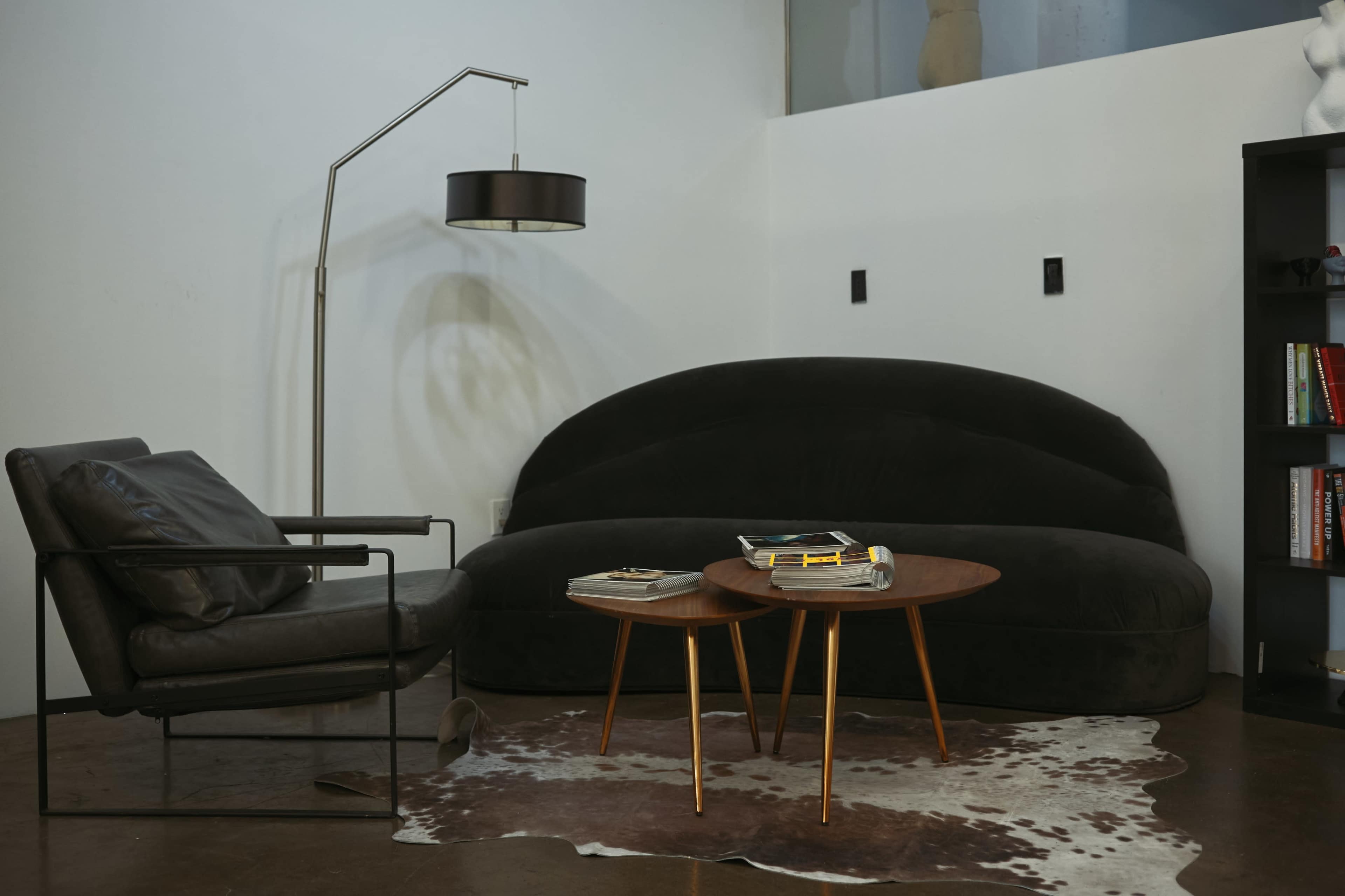 The image shows a modern living room setup featuring a curved black sofa, a sleek armchair, two wooden side tables, and a floor lamp.
