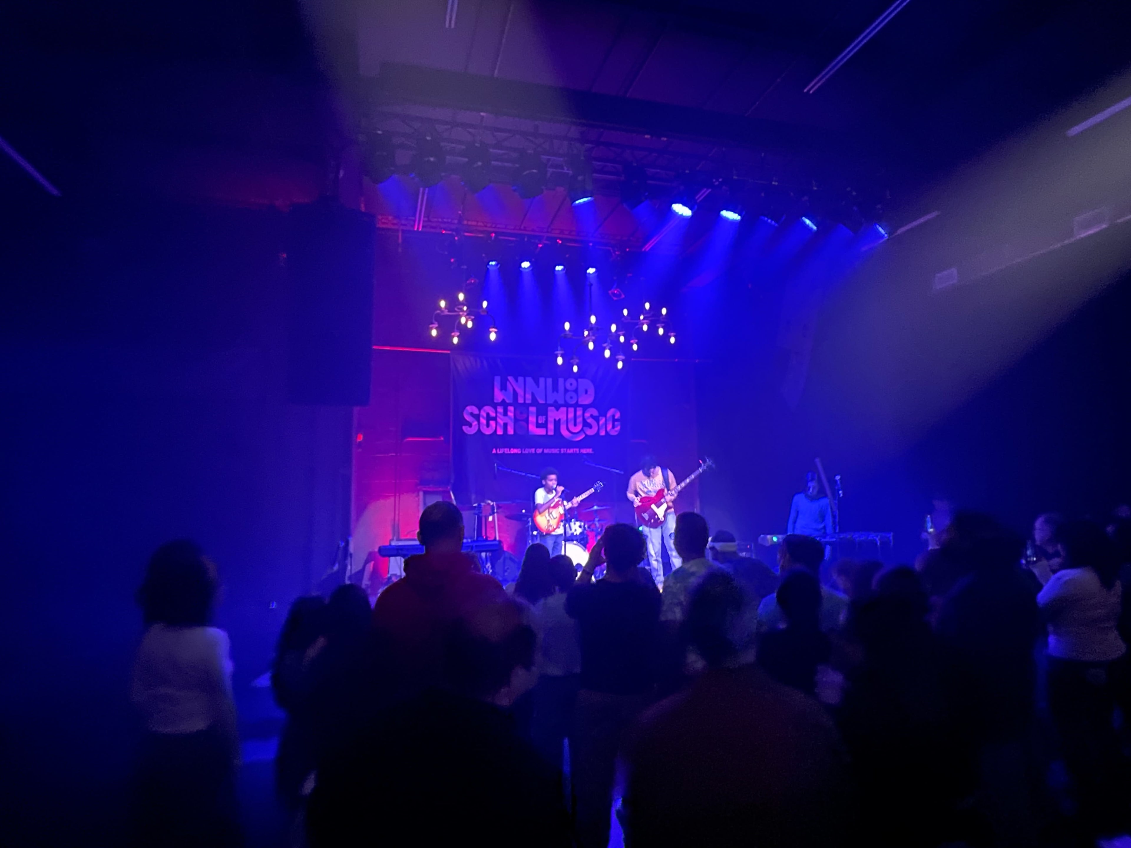 A band performs on stage in a dimly lit venue with an audience watching attentively.