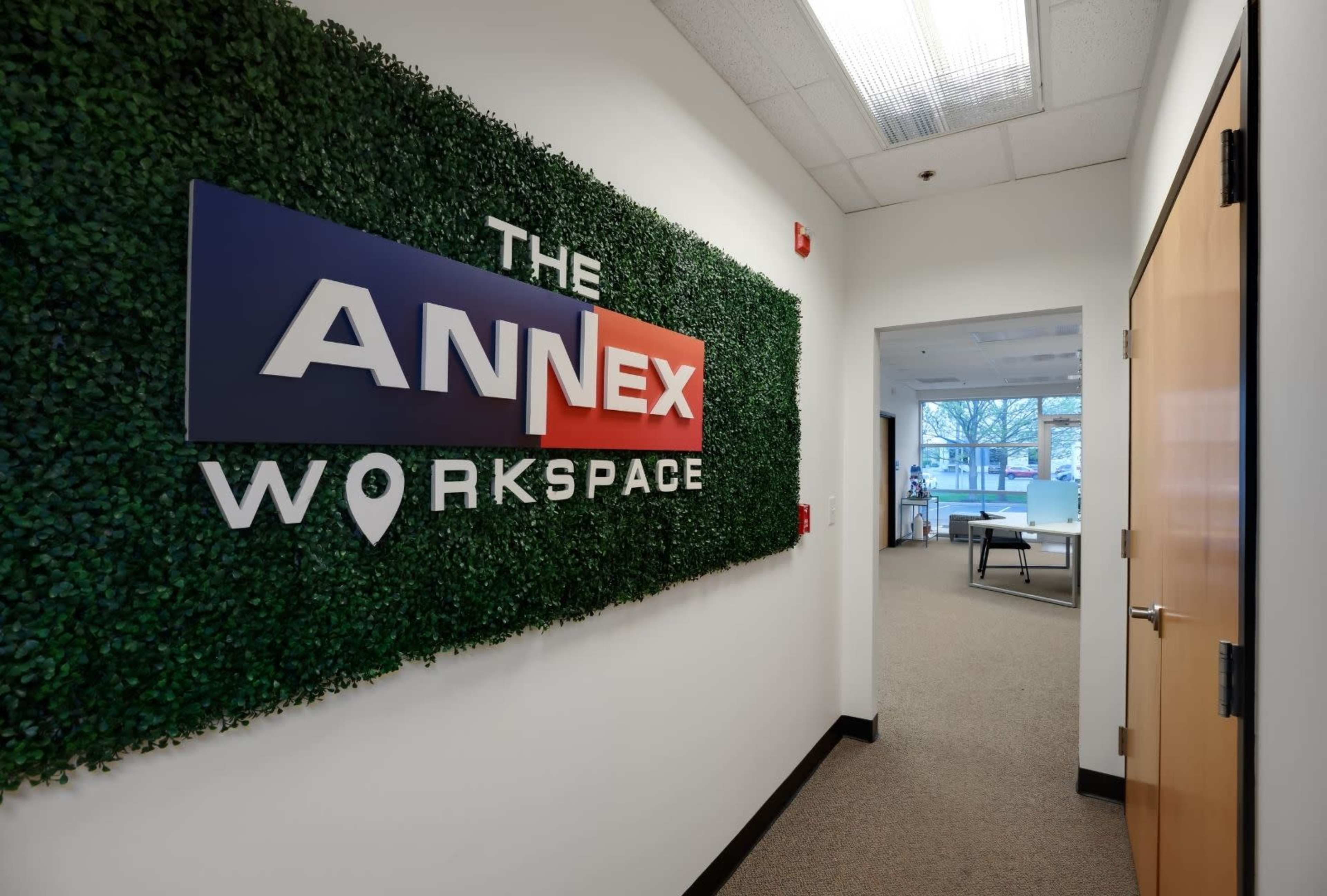 The image shows a hallway leading to a workspace, with a green wall feature displaying the sign "THE ANNEX WORKSPACE."