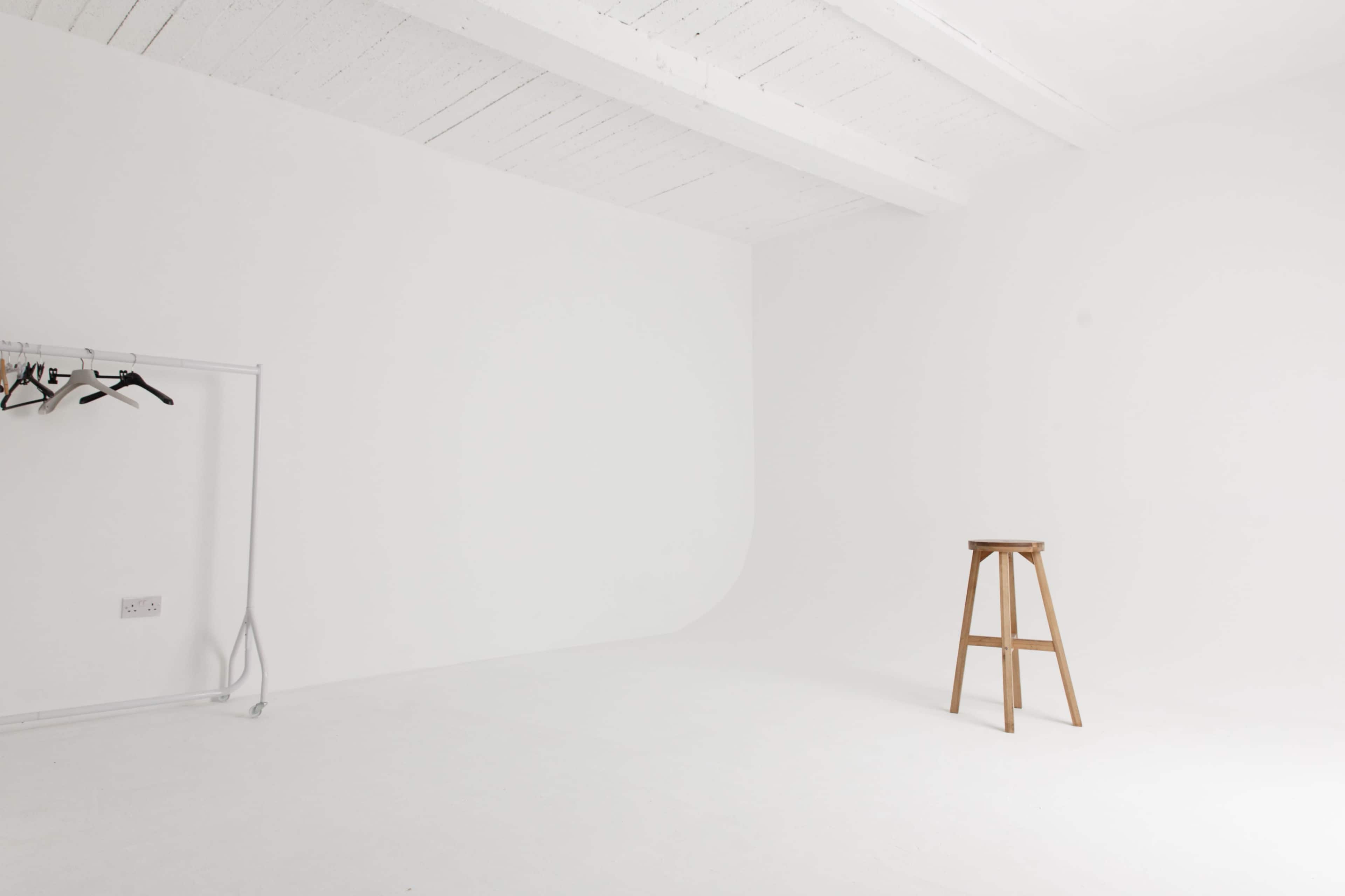 A minimalistic white room with a wooden stool and a clothing rack.