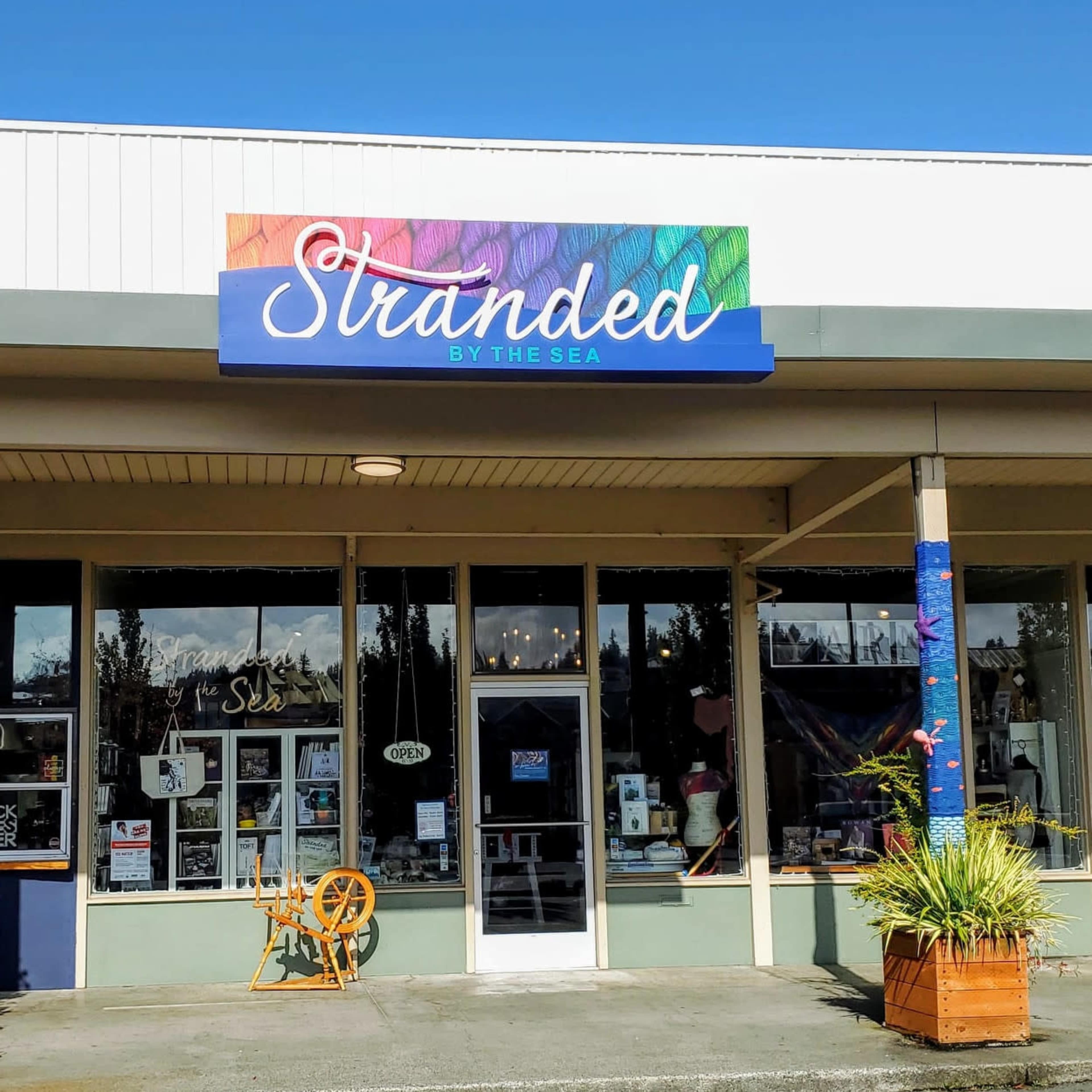 The image shows the storefront of a shop called "Stranded by the Sea," featuring large windows and a colorful sign above the entrance.