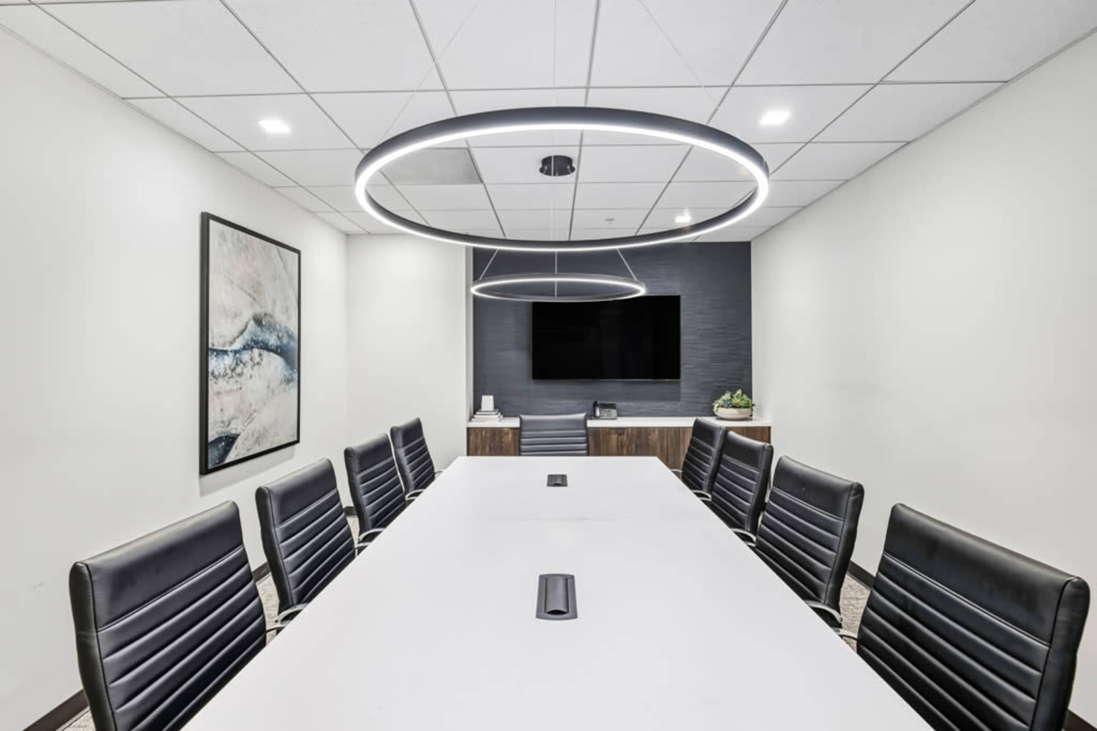 The image shows a modern conference room with a long white table, black leather chairs, and two circular light fixtures overhead.