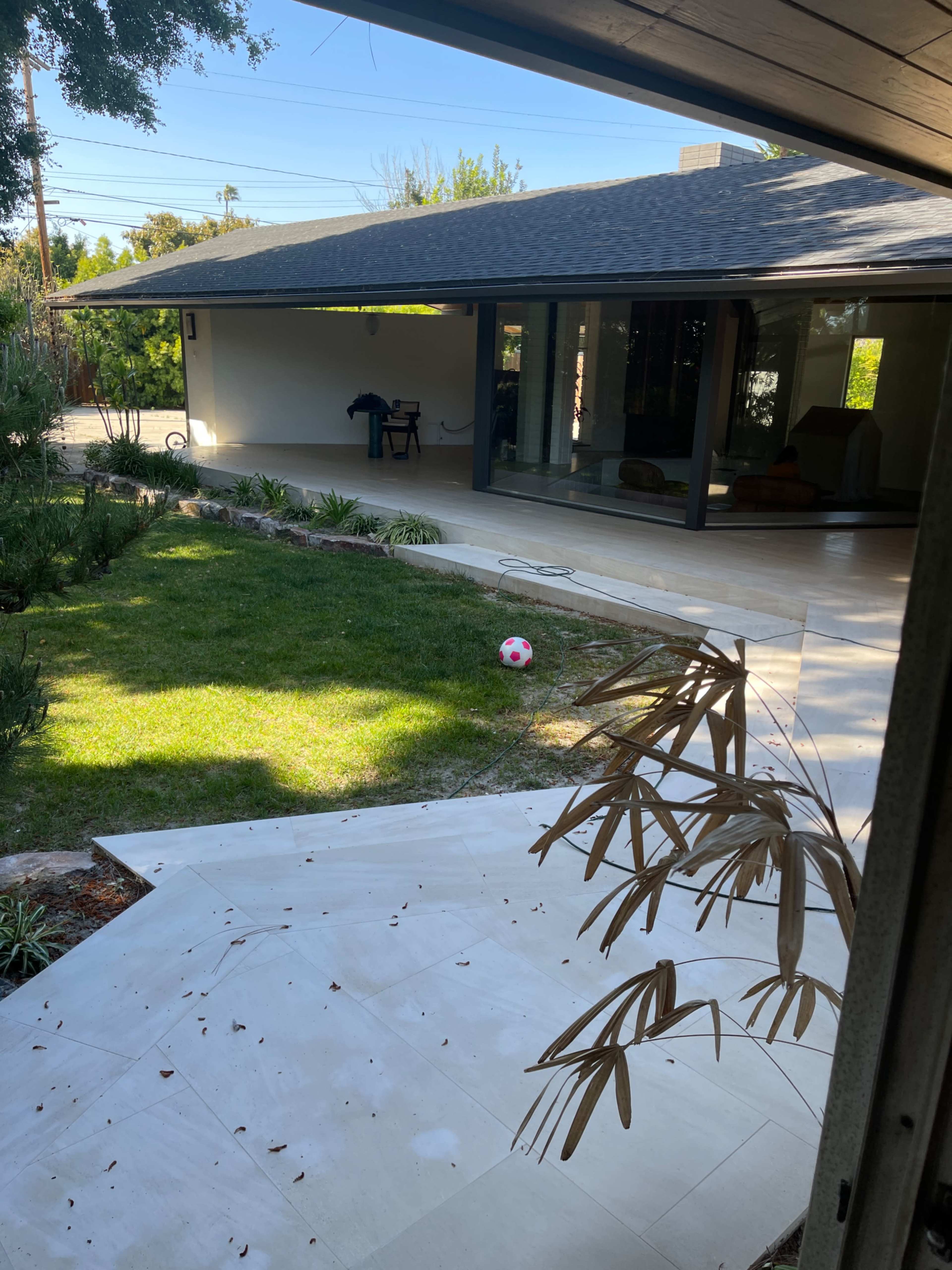 A pink and white soccer ball rests on the grass in a backyard setting with a modern house in the background.