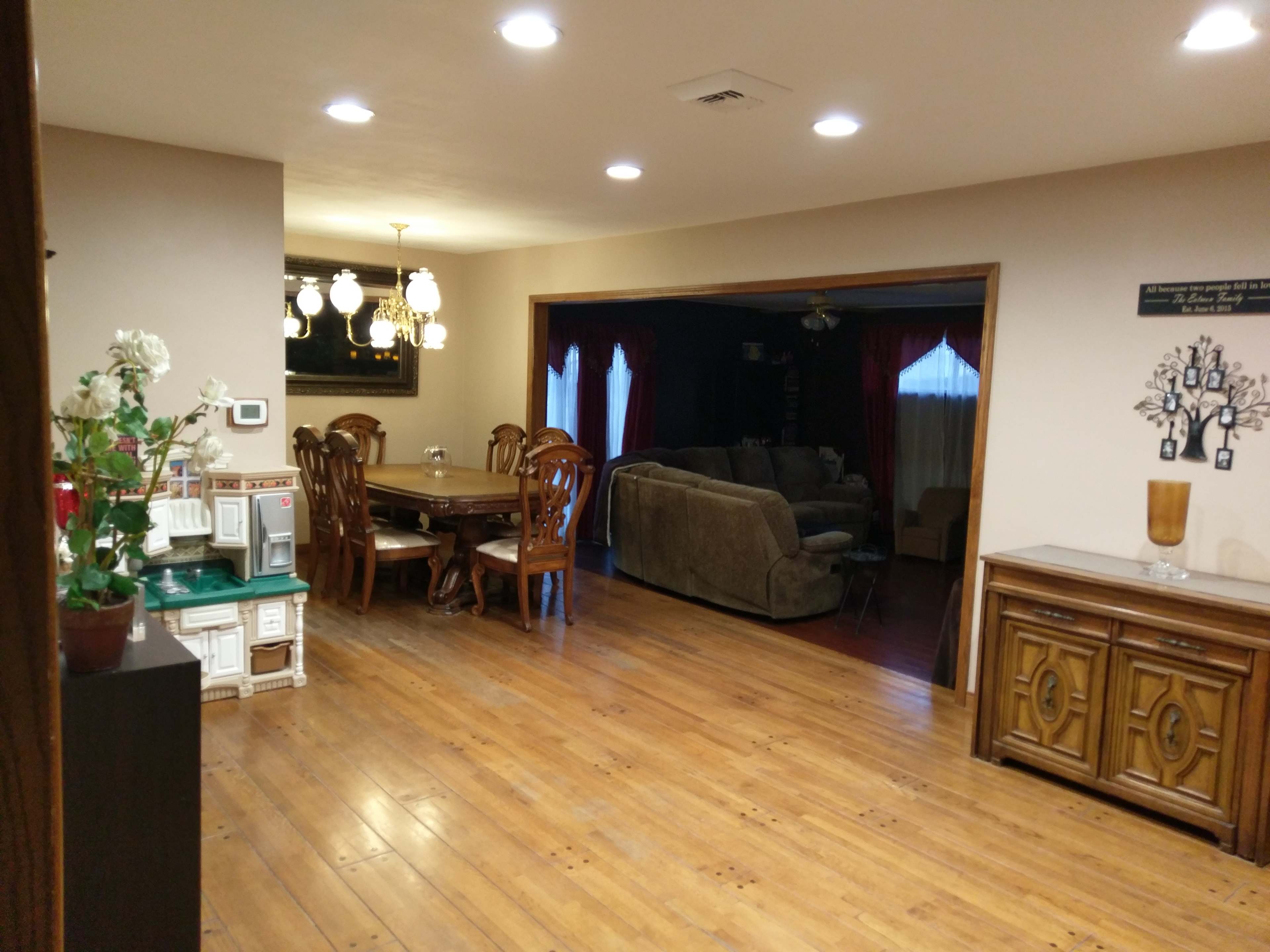 A spacious interior room with wooden flooring, featuring a dining area with a table and chairs, a living area with a couch, and a decorative sideboard.