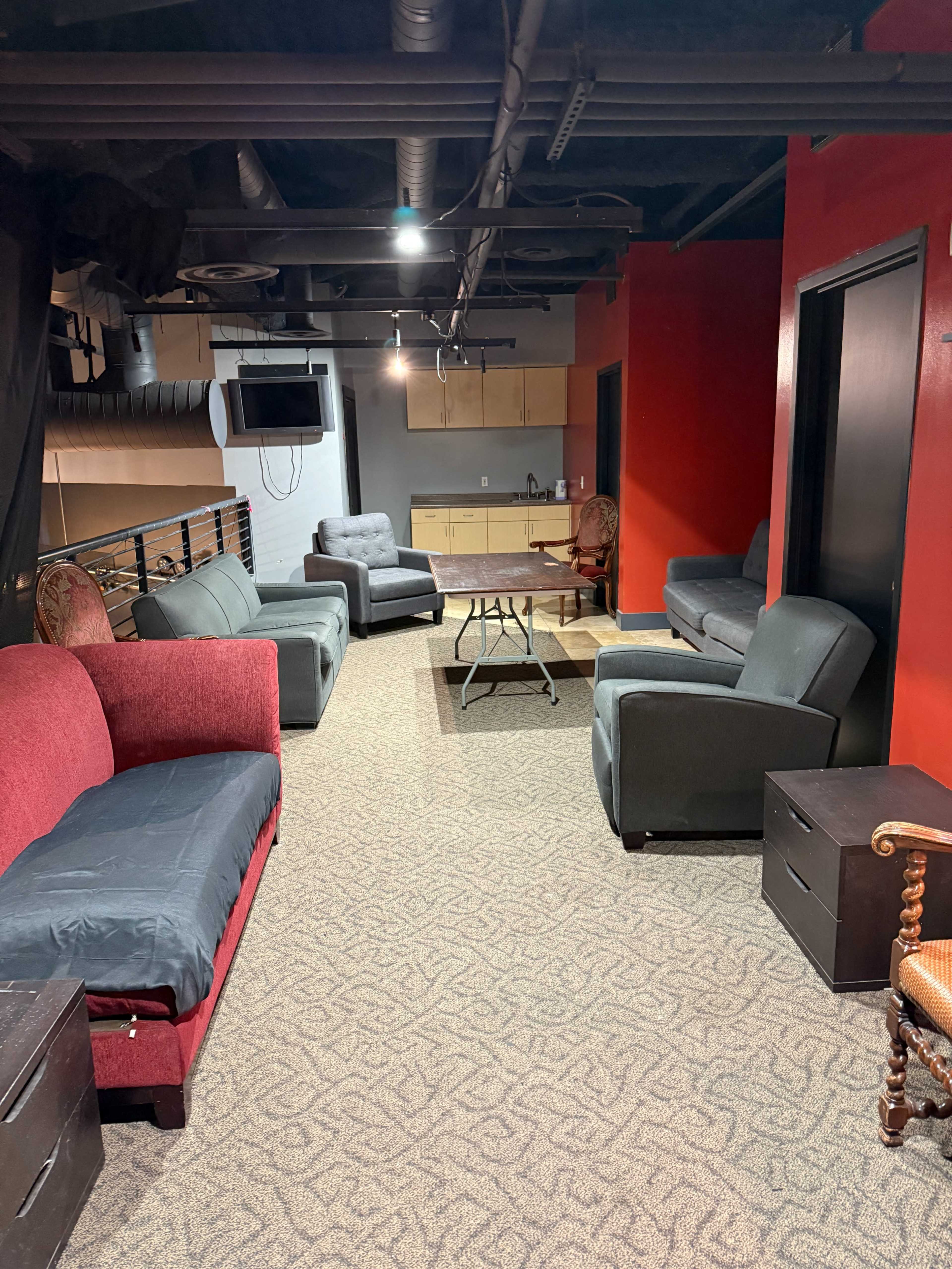 The image shows a lounge area with several couches, chairs, and small tables arranged on a carpeted floor beneath low ceilings.