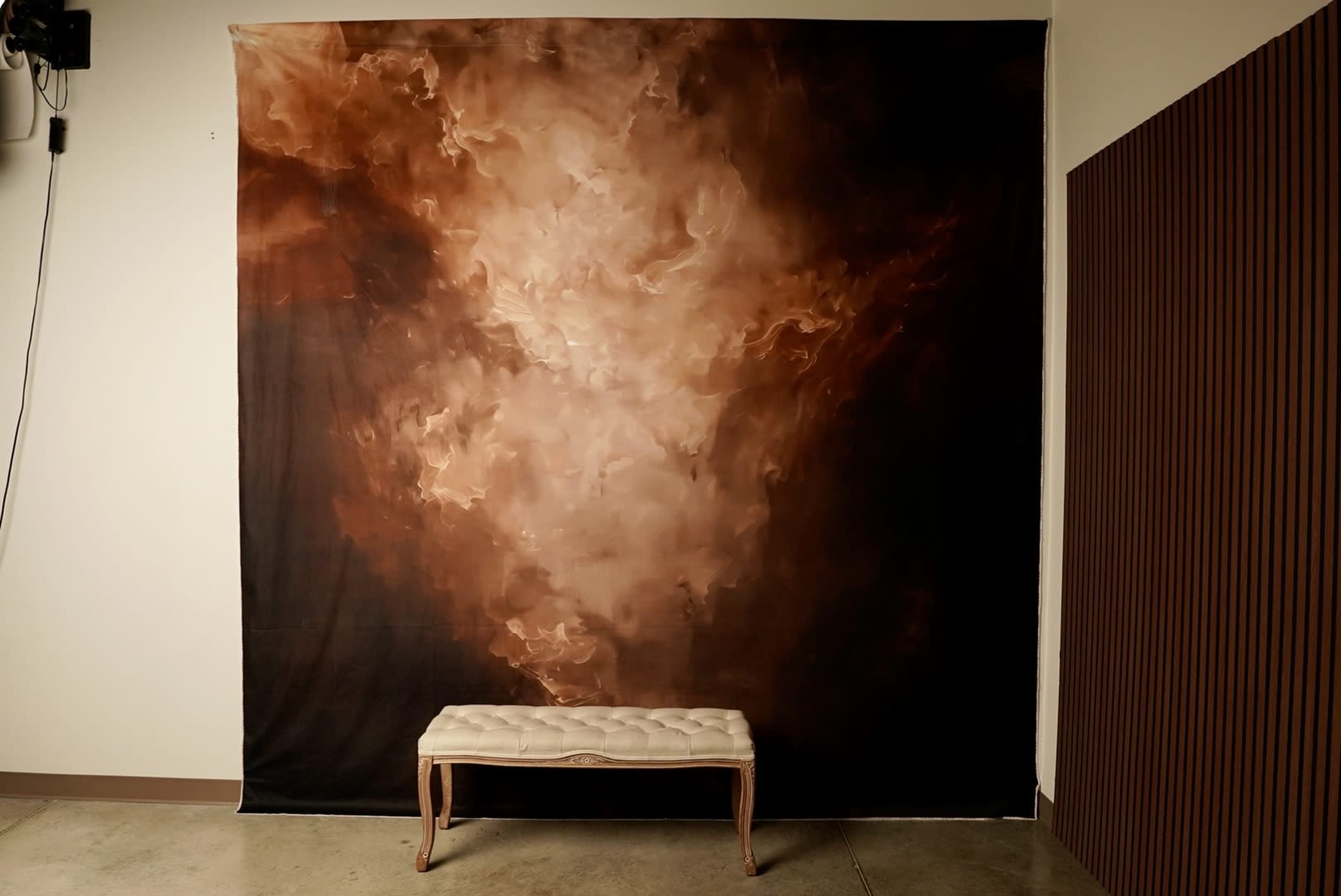 A large fabric backdrop with swirling brown and cream colors hangs on the wall behind a light-colored bench.