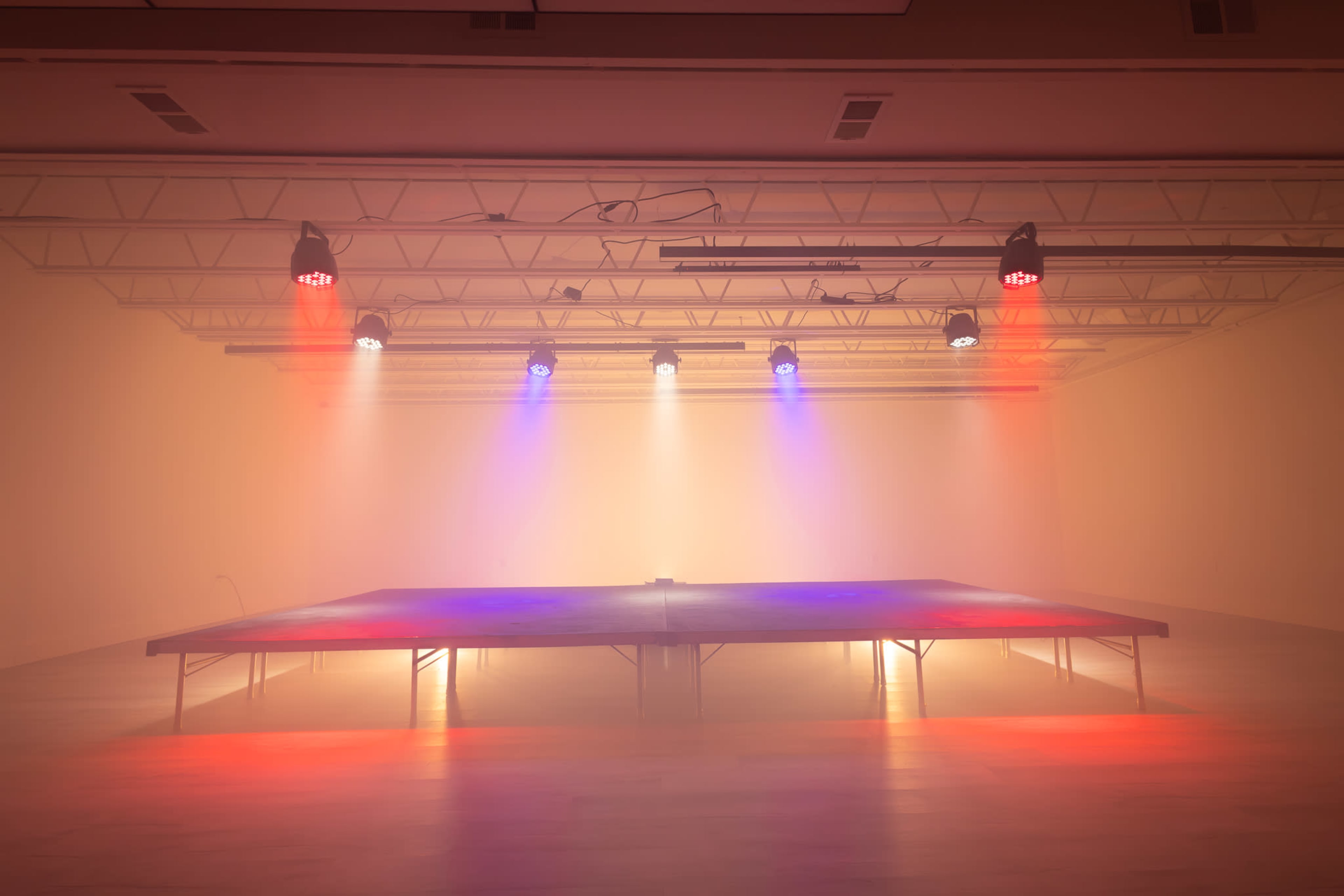 A large performance stage is illuminated by colorful lights in a foggy indoor setting.