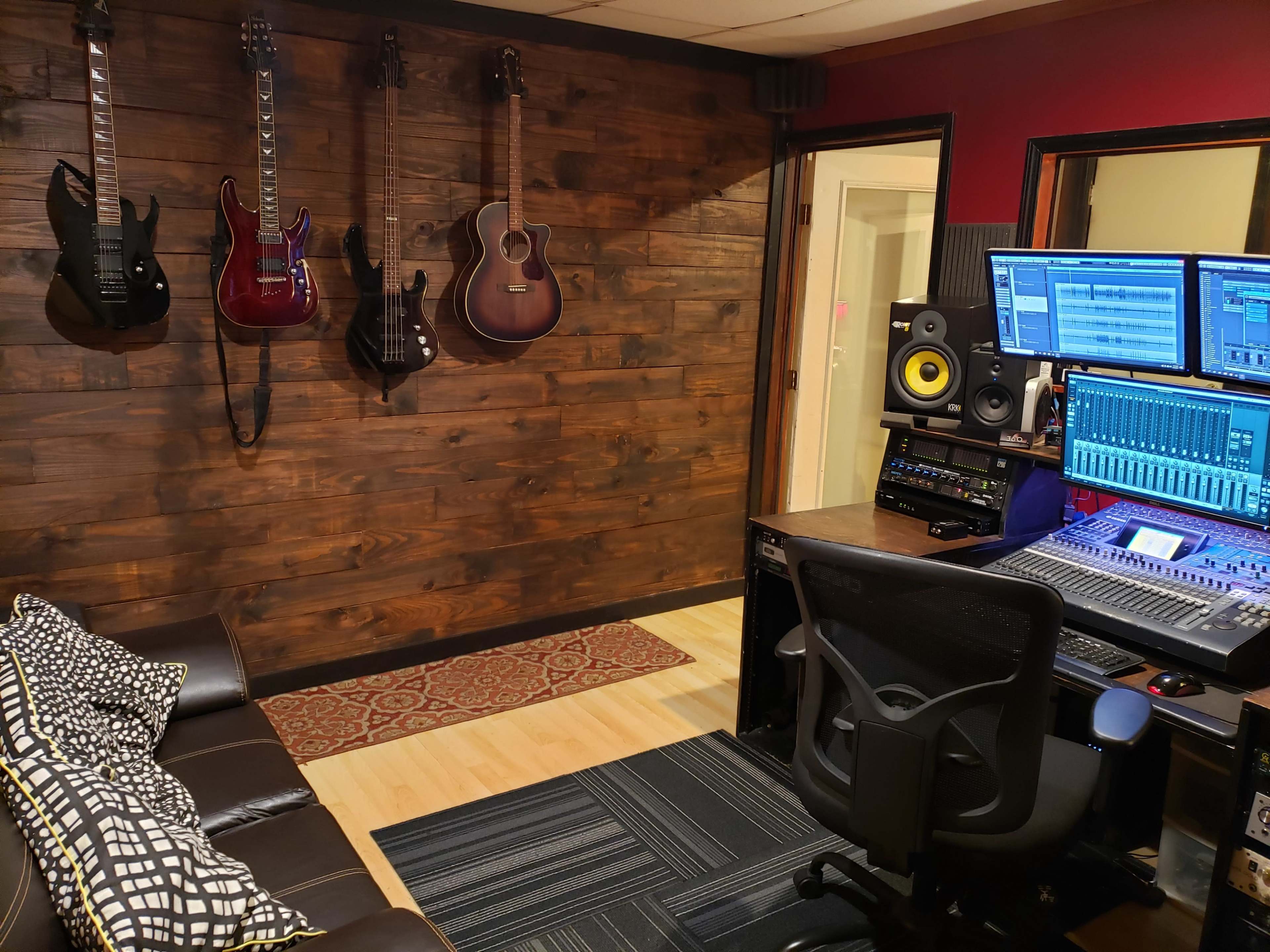 A music production studio features a wall adorned with guitars, a mixing console, and a comfortable seating area.