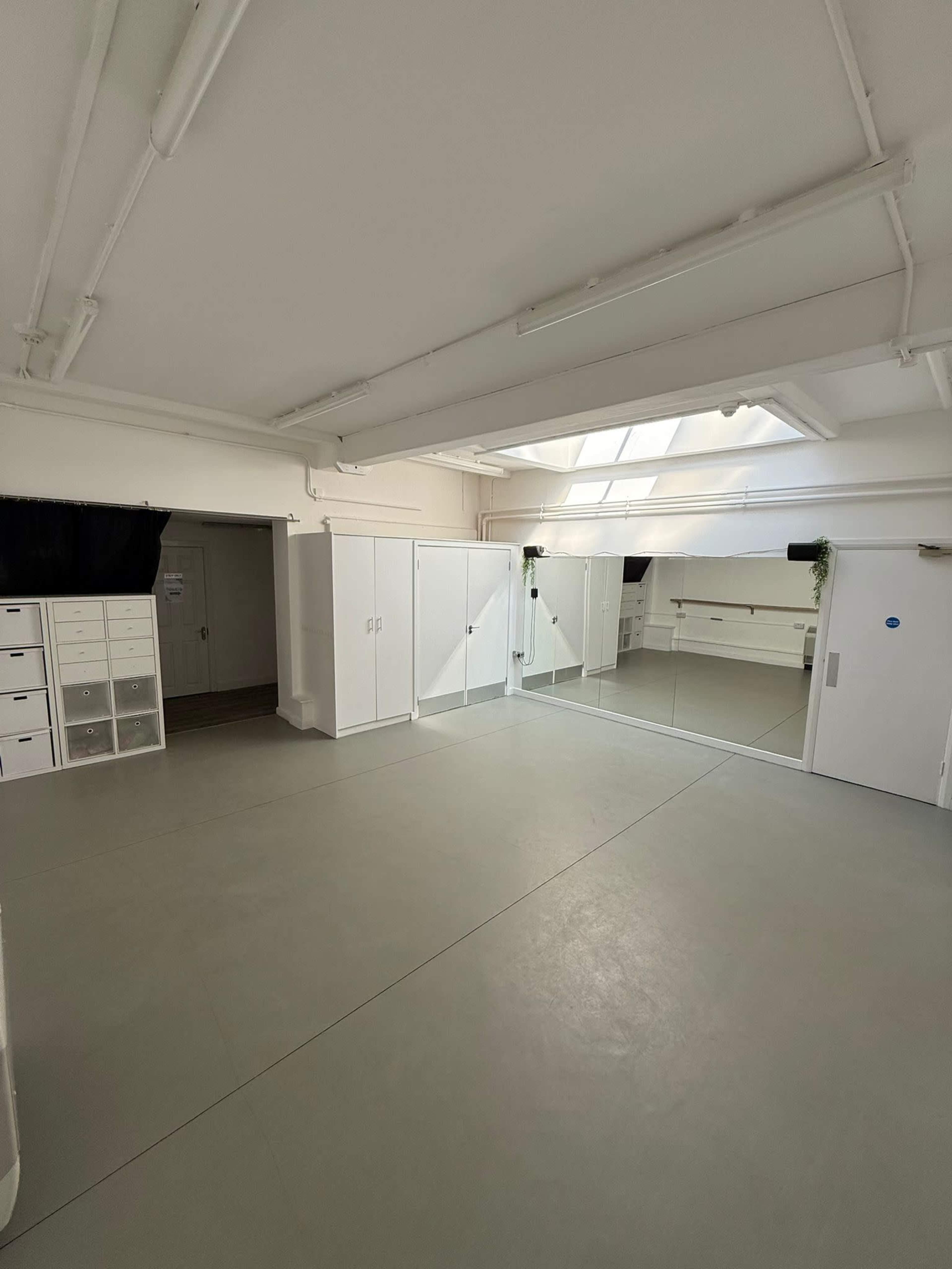 The image shows a well-lit, minimalist room featuring large mirrors, white cabinetry, and a skylight.