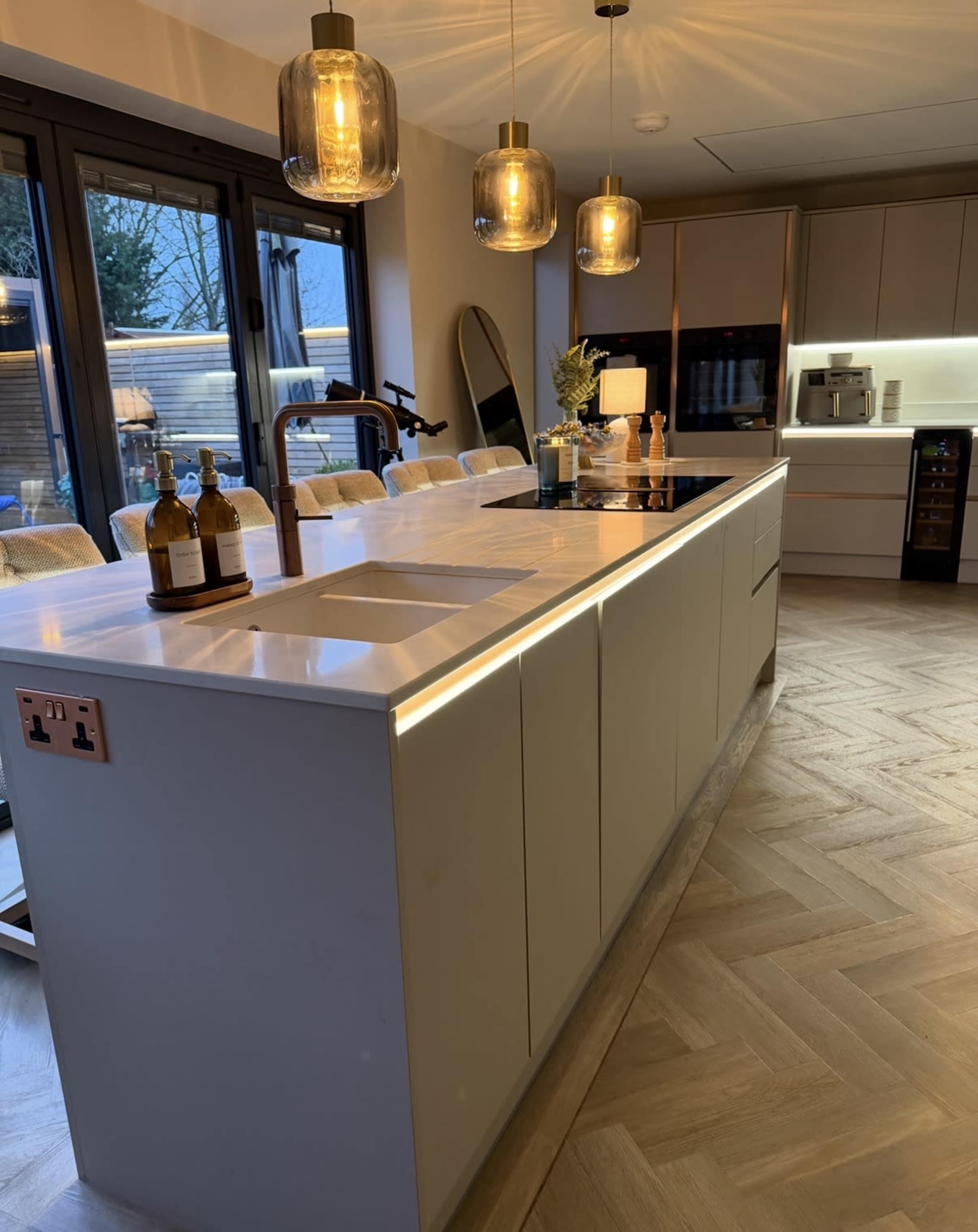 The image shows a modern kitchen with a large island, pendant lights, and a sleek design featuring a neutral color palette.