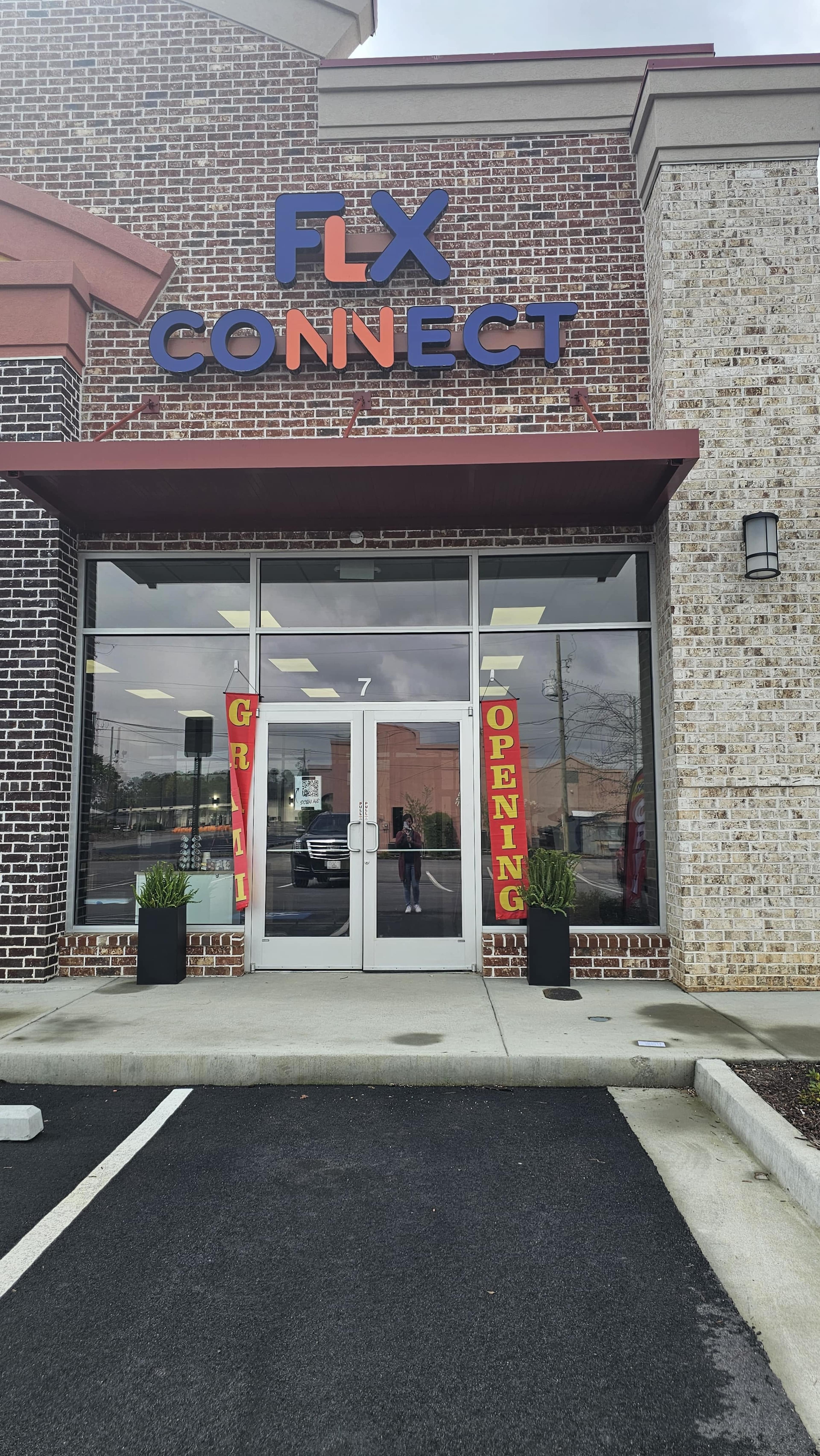 The storefront of FLX Connect features a "Grand Opening" sign and is adorned with potted plants near the entrance.