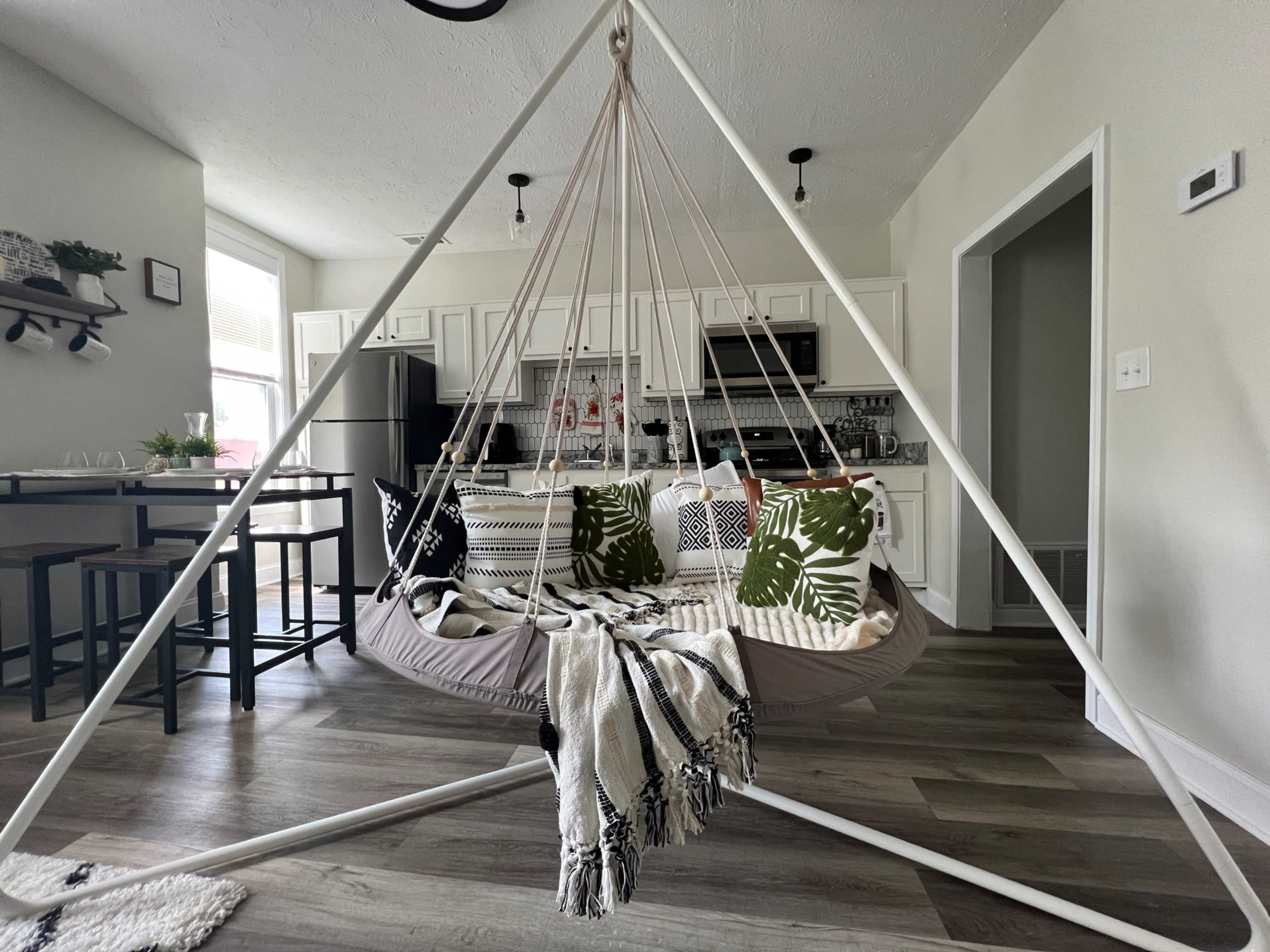 A triangular hanging chair with patterned cushions in a light-filled kitchen and dining area.