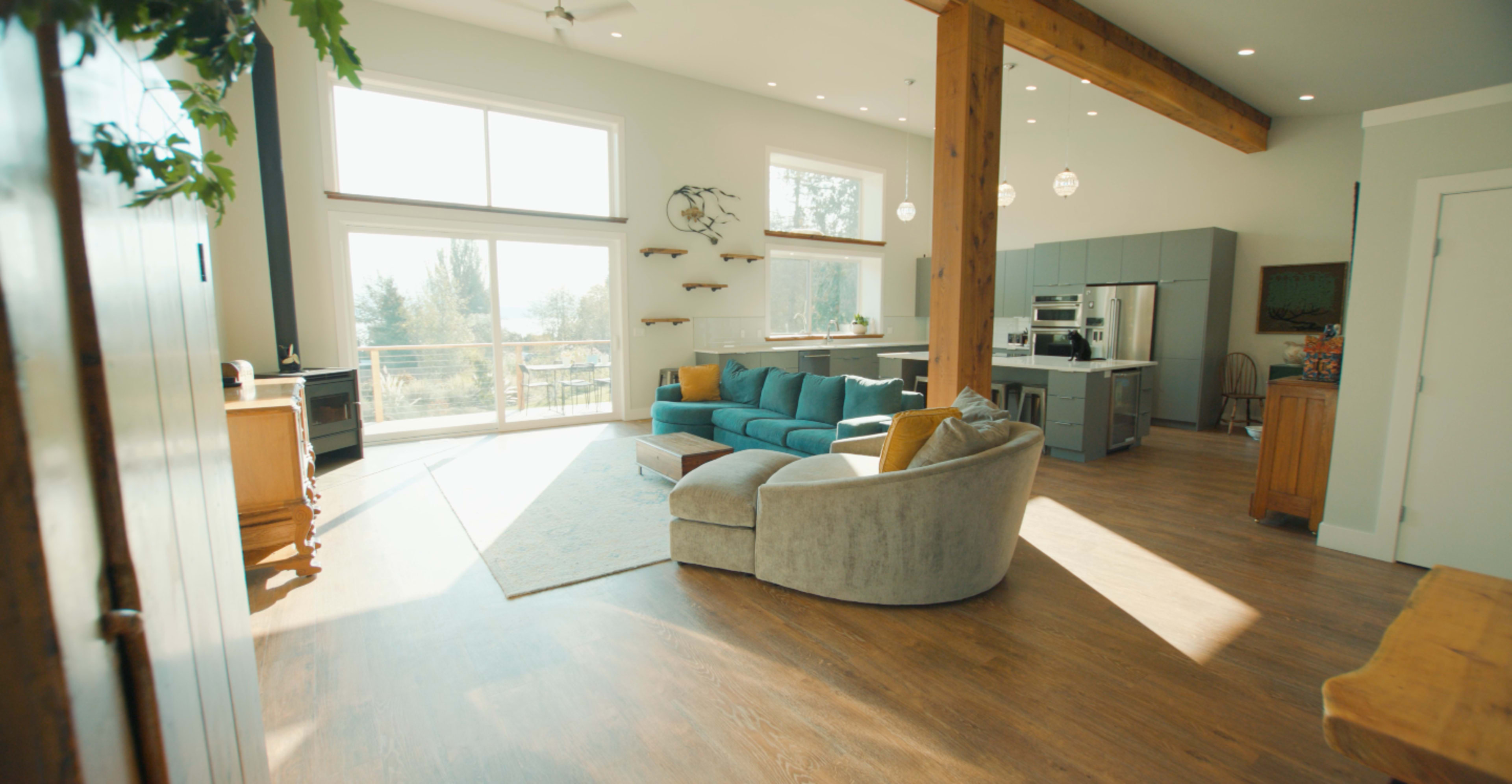 A spacious living area with large windows, a blue sectional sofa, and a kitchen area featuring modern appliances.