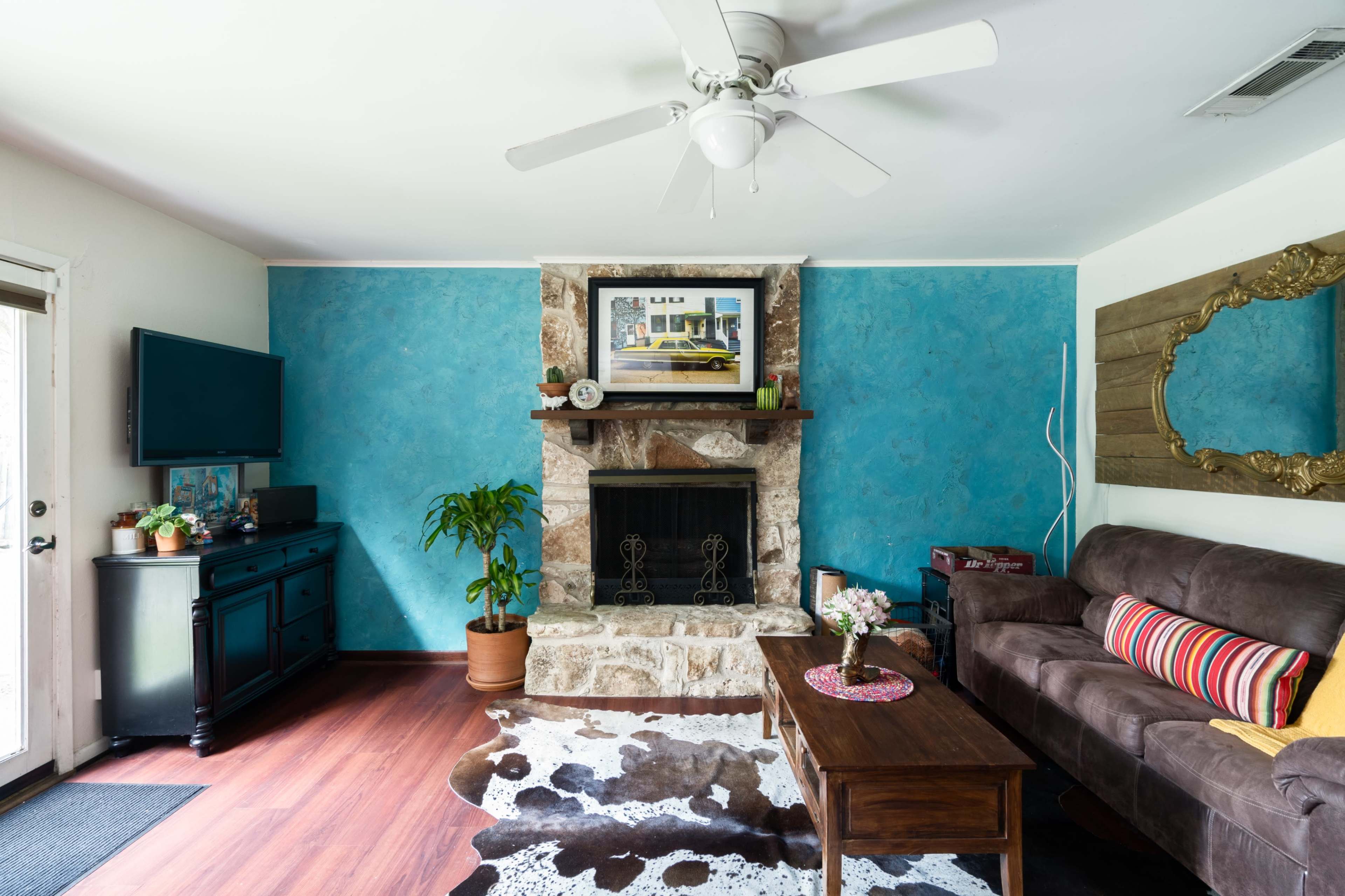 The living room features a stone fireplace with a colorful painting above it, a brown couch, a wooden coffee table, and blue walls.