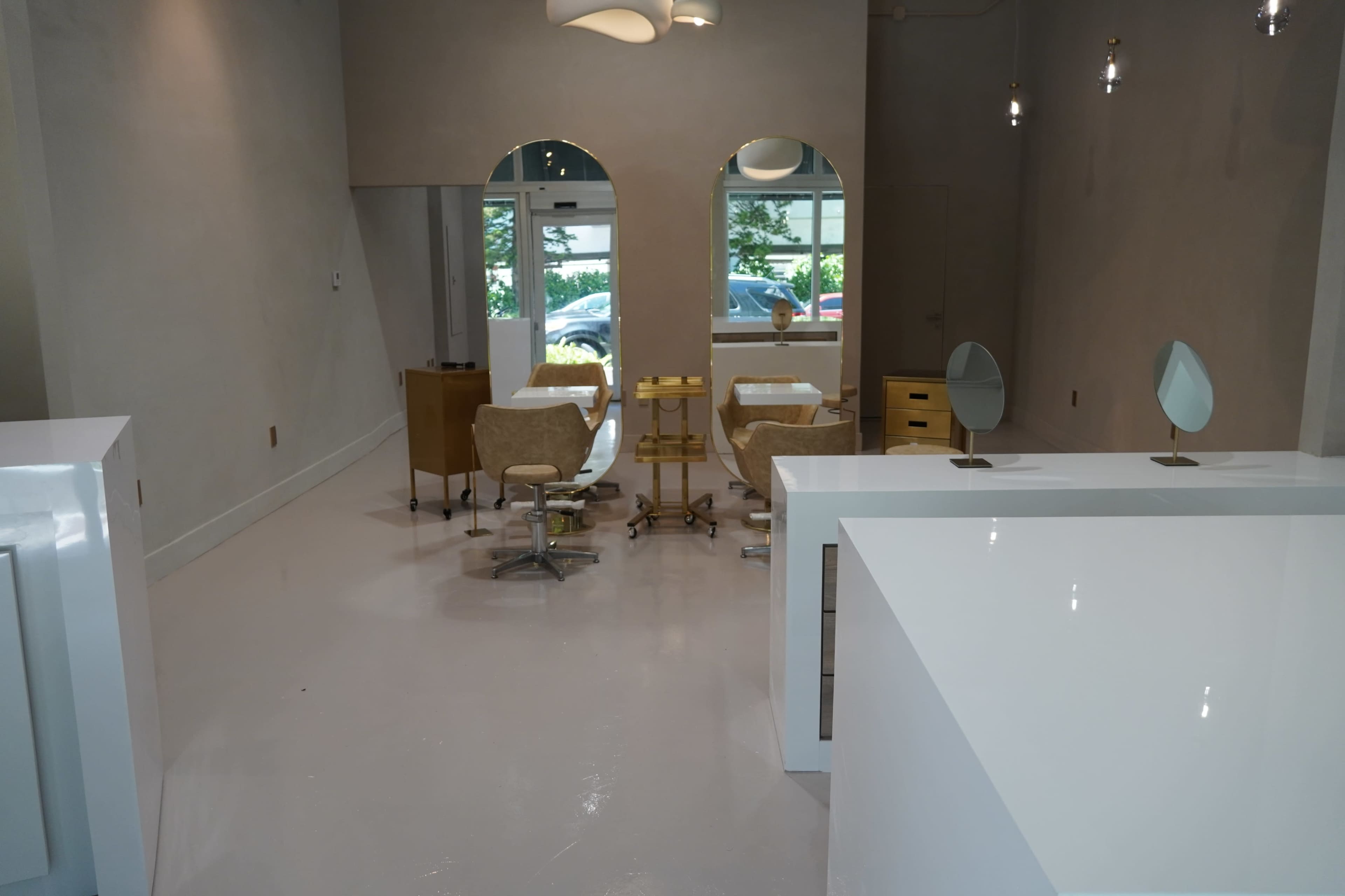 The image shows a modern salon interior featuring two styling chairs, a set of mirrors, and a reception area with minimalistic furnishings.