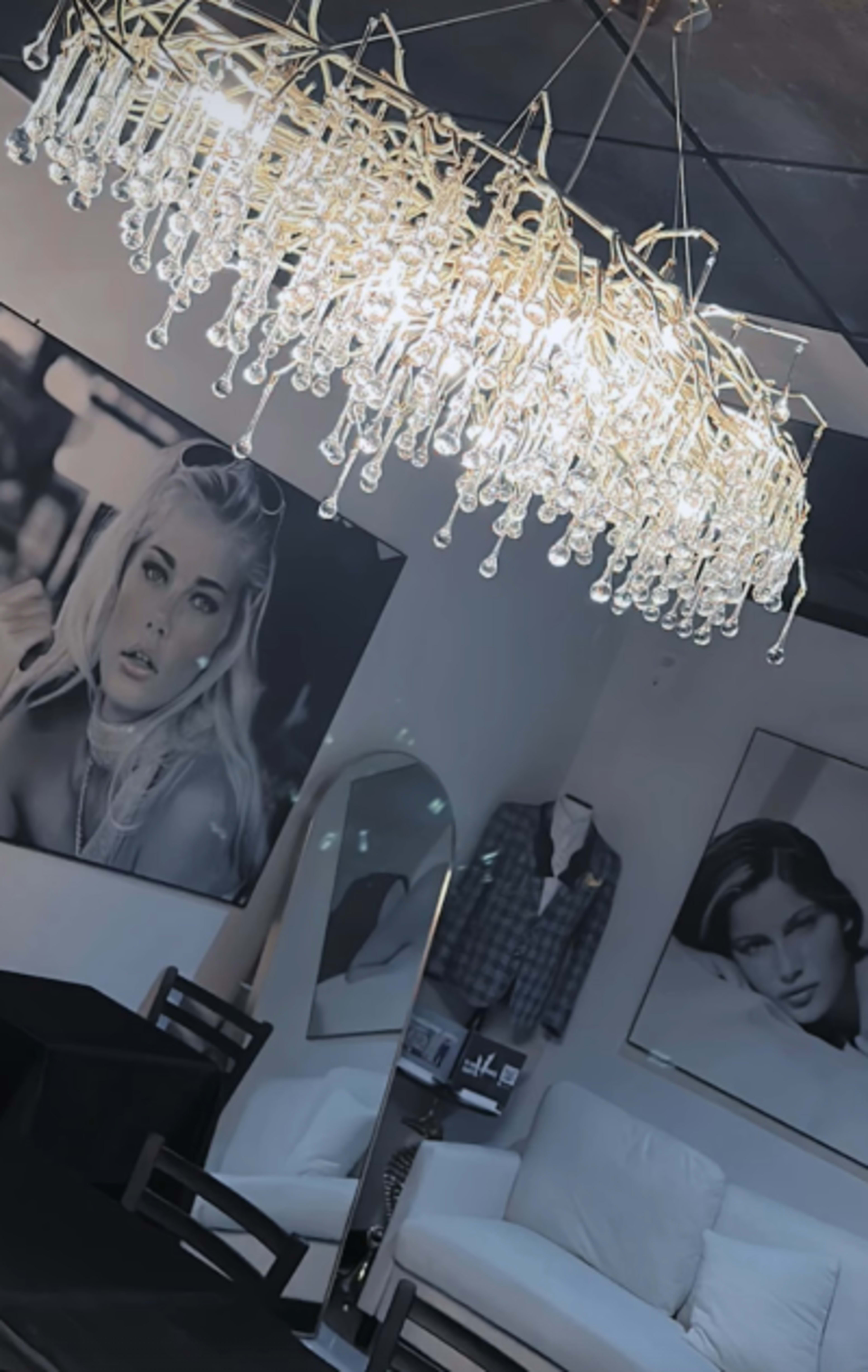 A modern dining area features a large chandelier with crystal droplets, framed black-and-white portraits on the walls, and minimalistic furniture.
