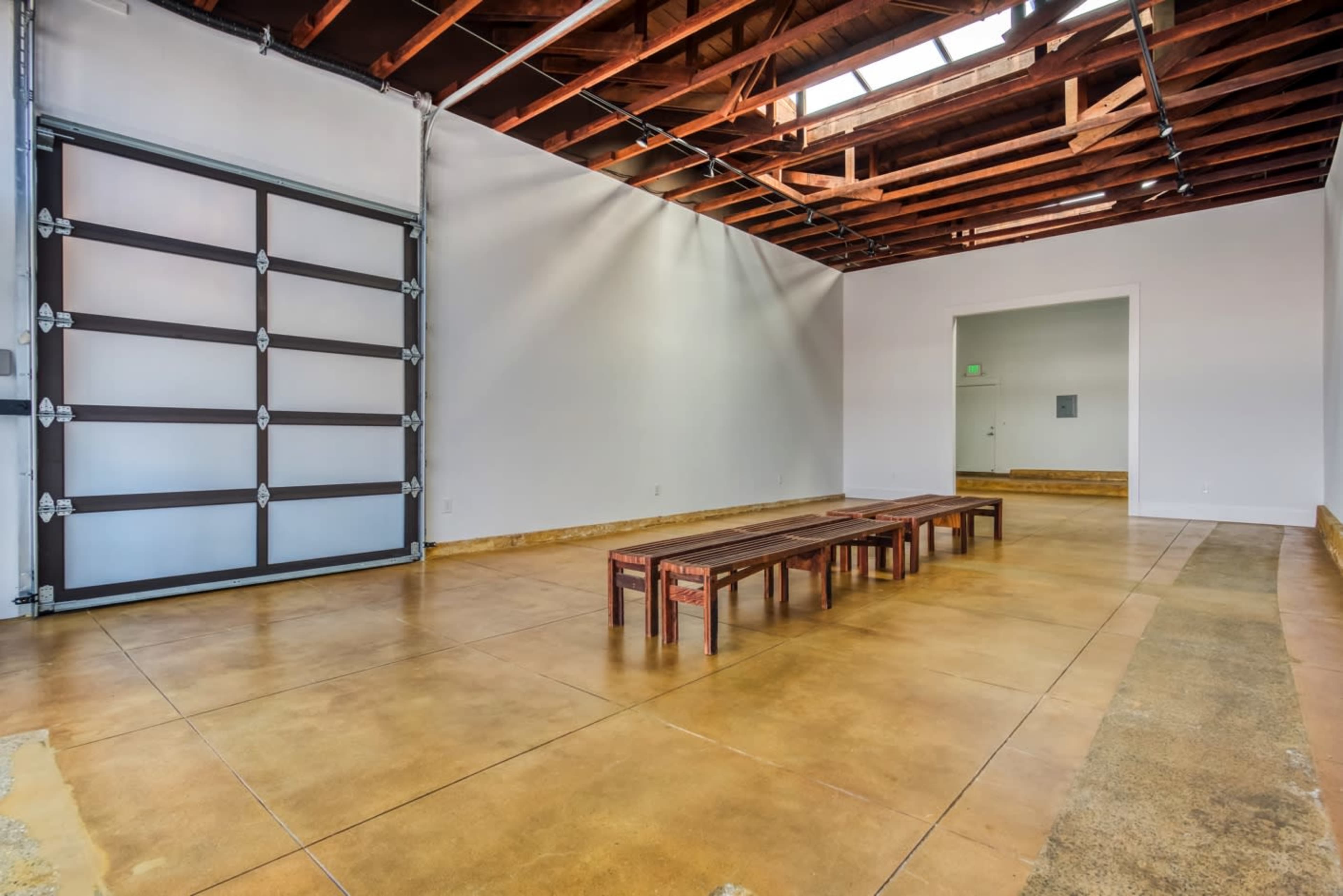A spacious room with polished concrete floors, wooden beams on the ceiling, and a set of wooden benches in the center.