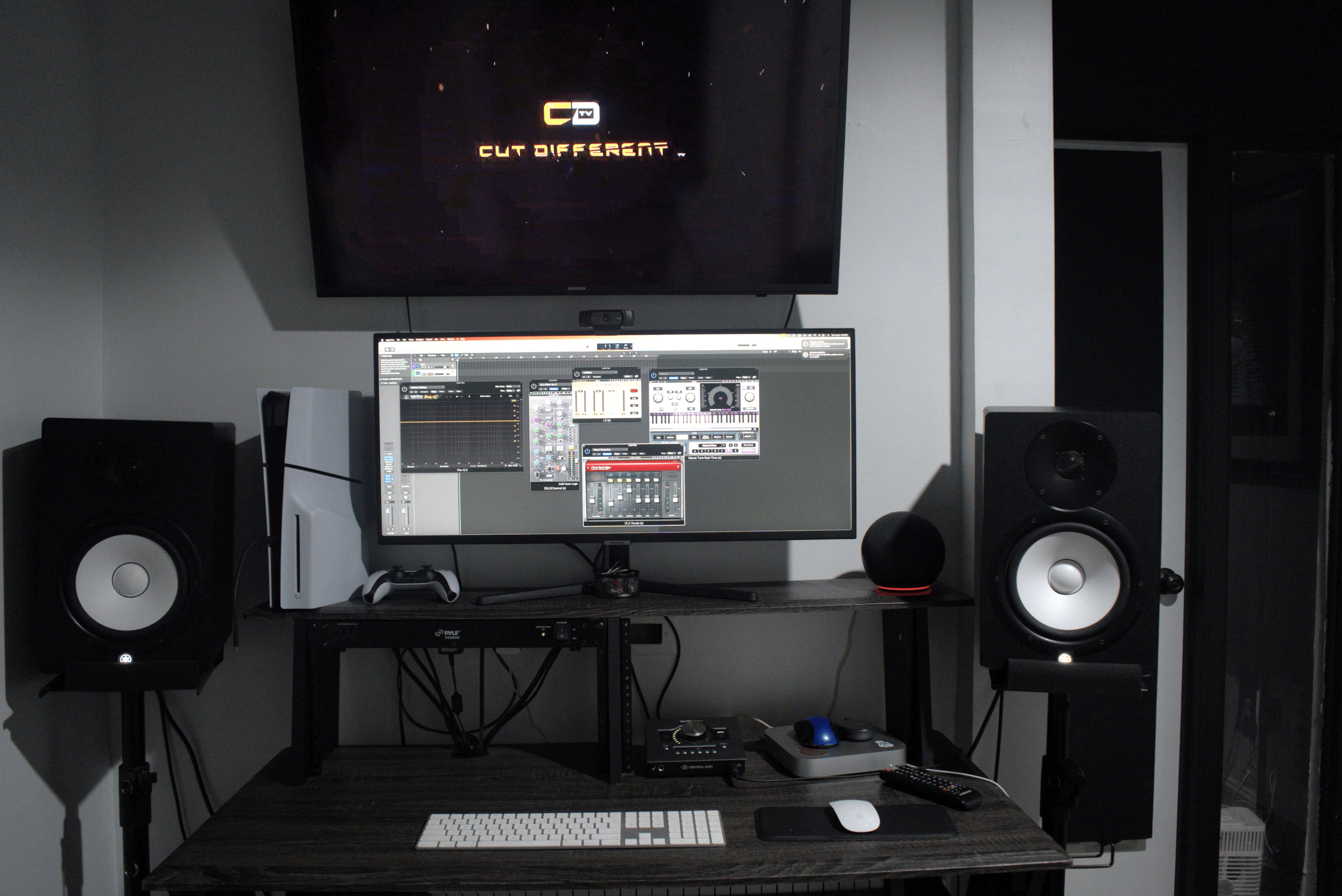 A computer workstation set up for music production features a large monitor displaying audio software, flanked by studio speakers and a keyboard.
