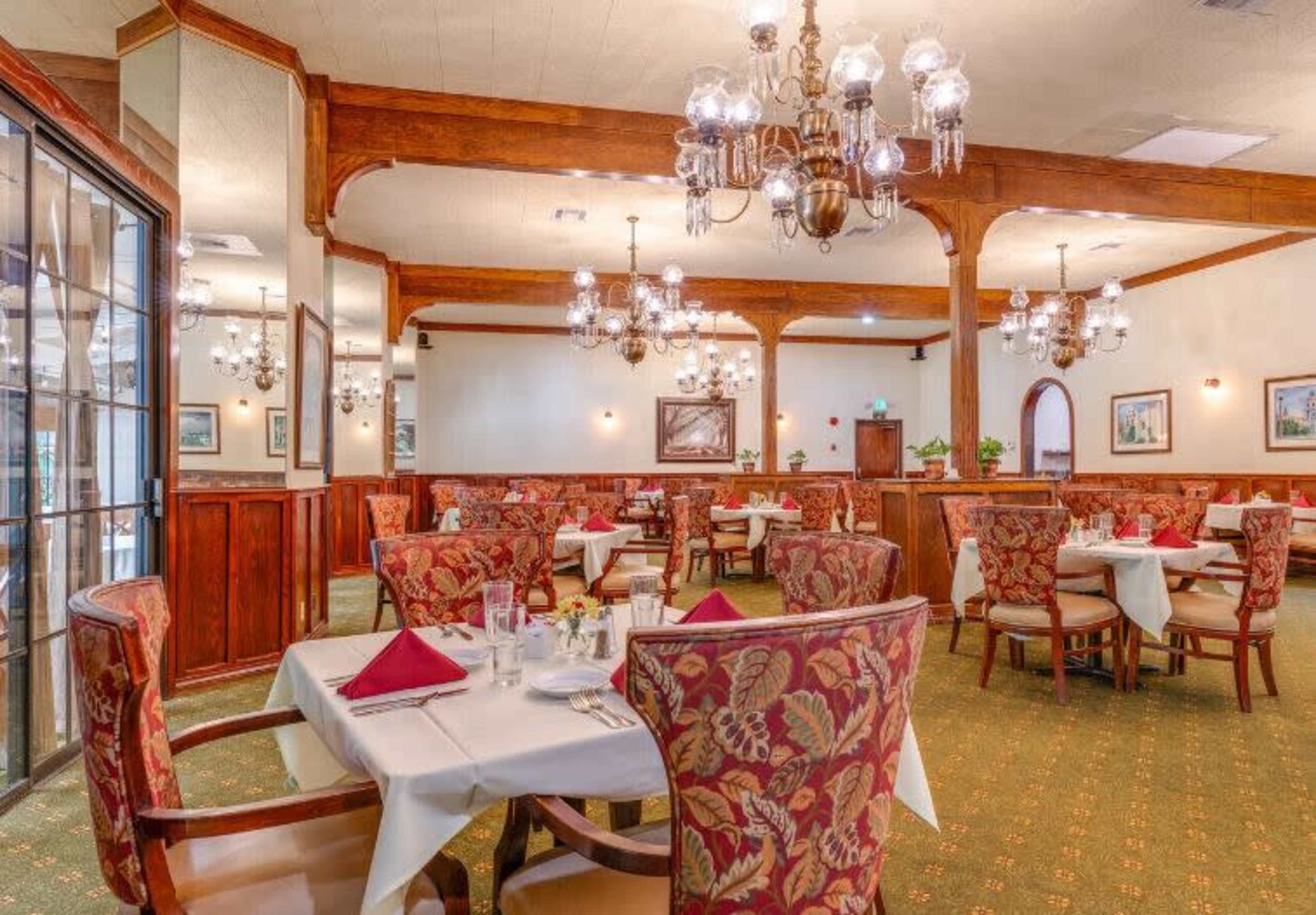 The image shows a dining area in a restaurant with neatly set tables, elegant chandeliers, and wood-paneled walls.