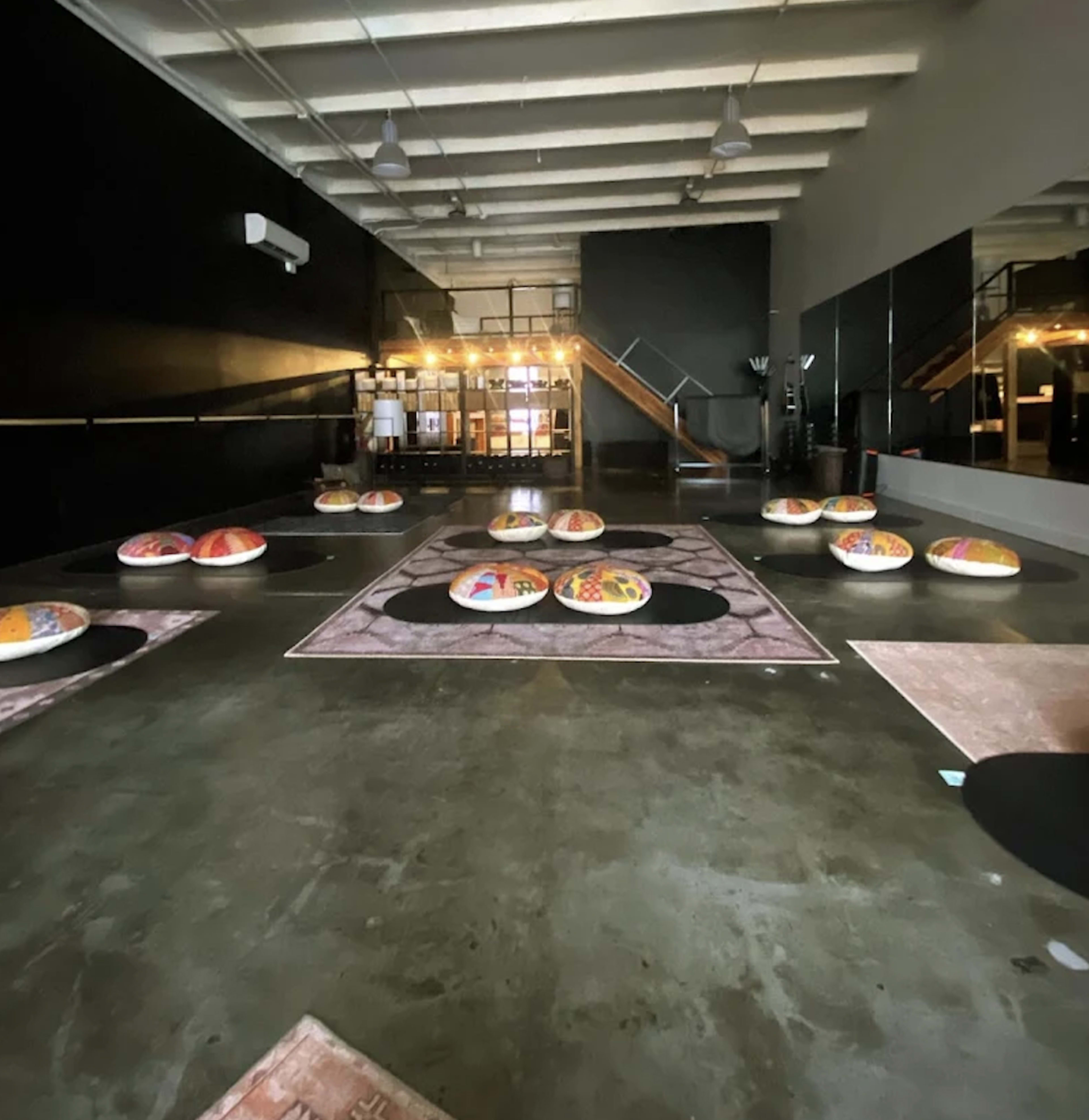 The image shows a spacious room with a polished concrete floor, featuring circular seating arrangements on large decorative rugs, illuminated by ambient lighting.