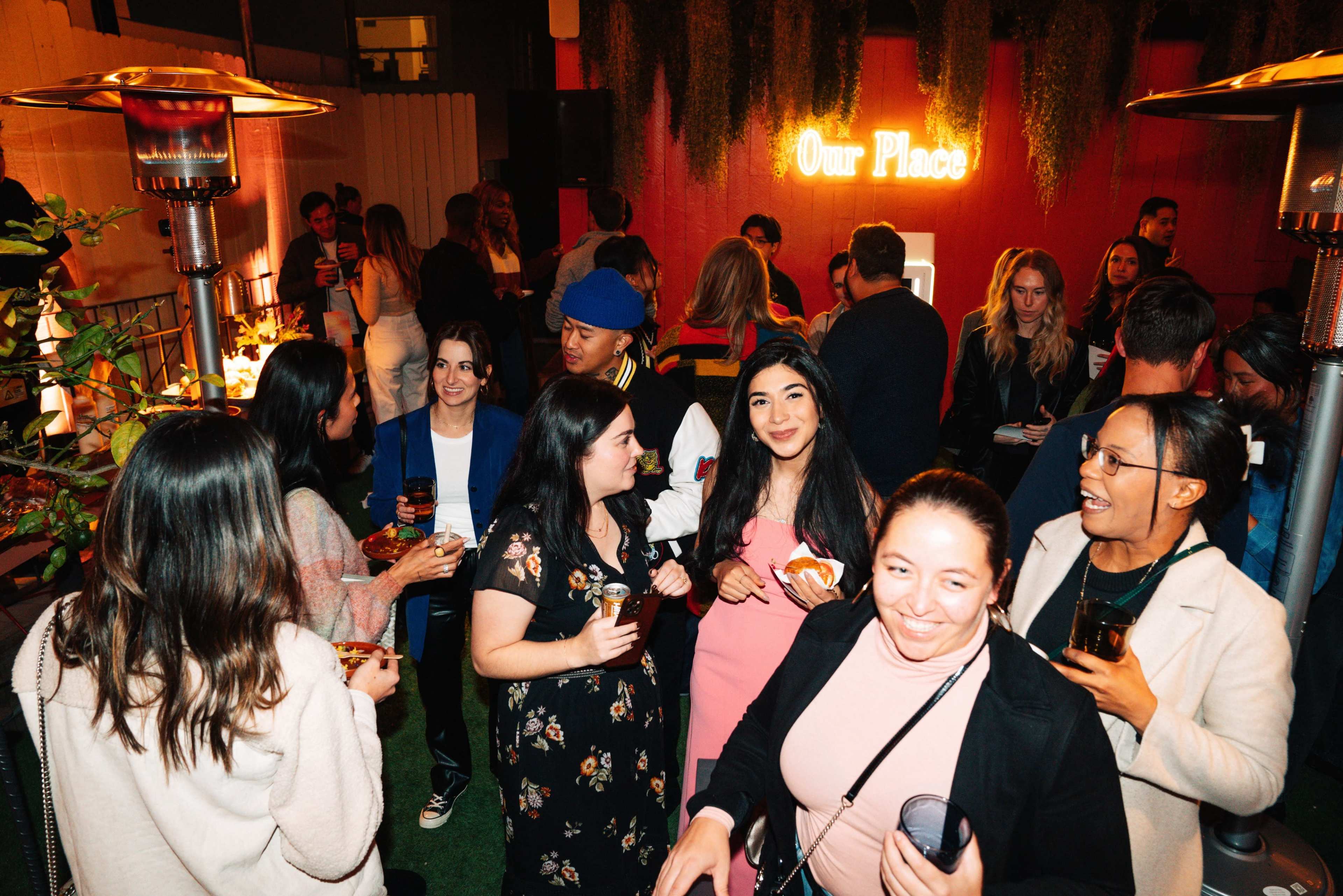 A crowded indoor gathering features people socializing and enjoying drinks under warm lighting.