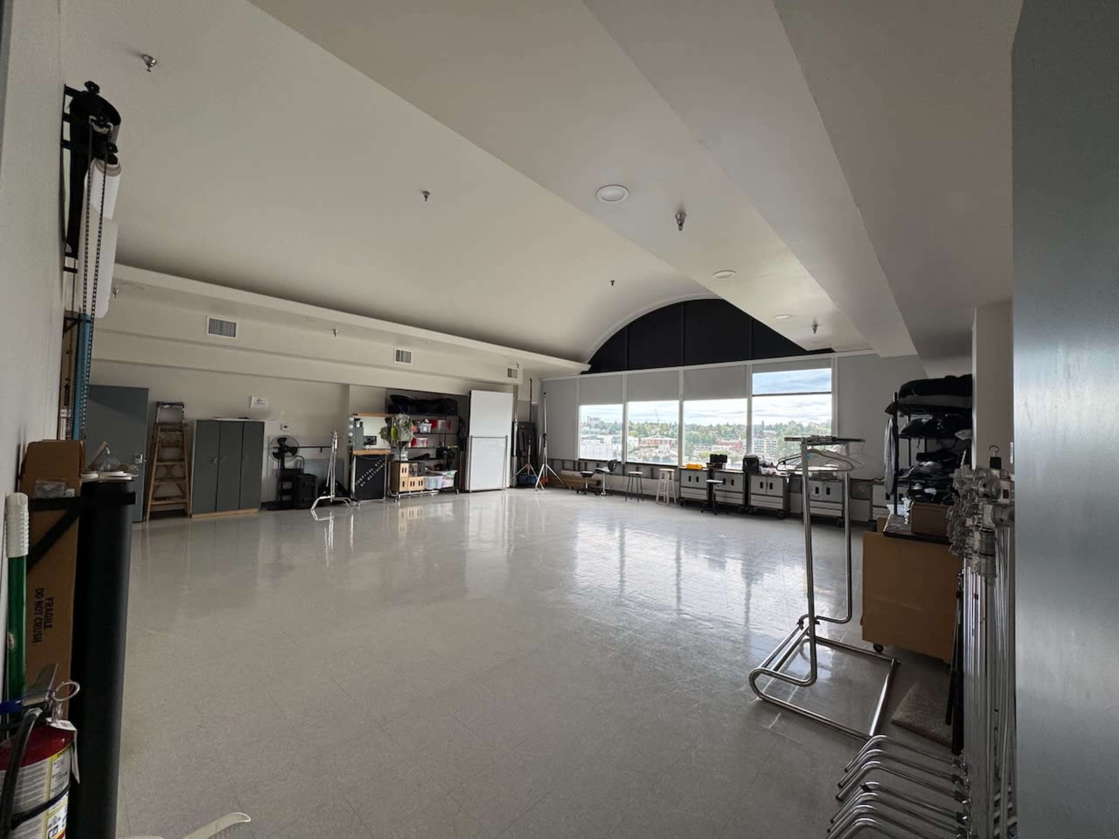The image shows a spacious, well-lit room featuring large windows, storage cabinets, and various equipment along the walls.