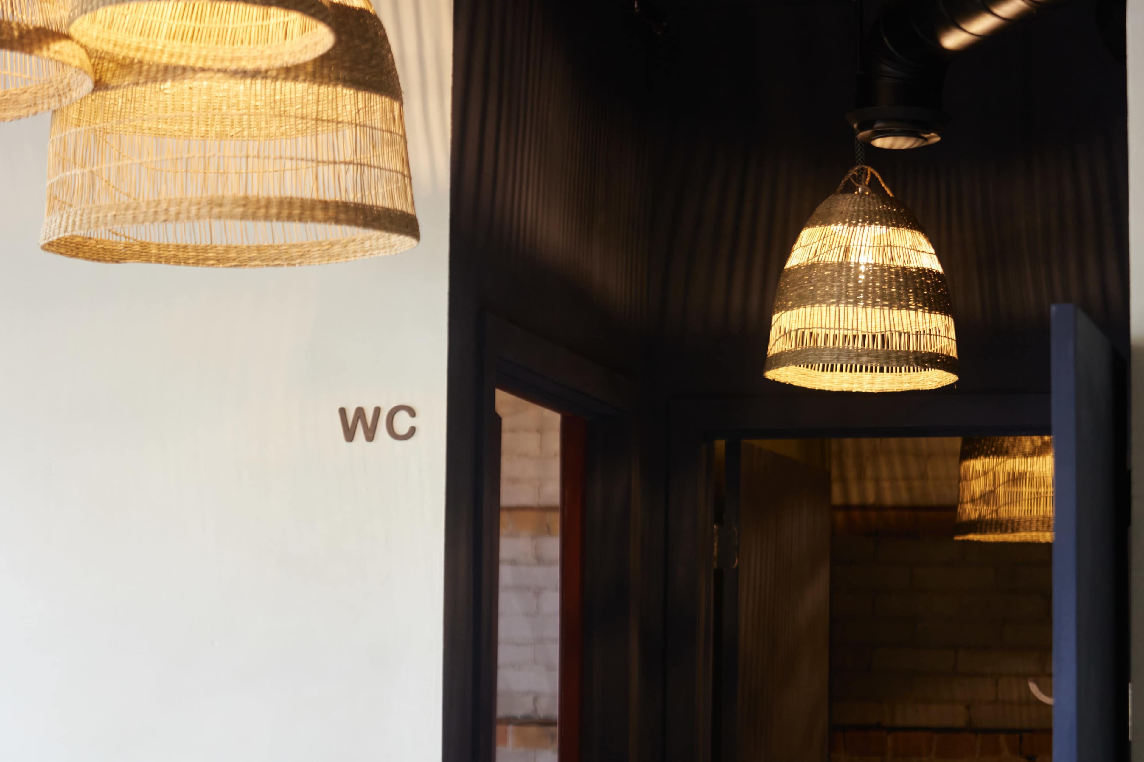 A hallway features woven pendant lights and a sign indicating "WC" next to an open door.