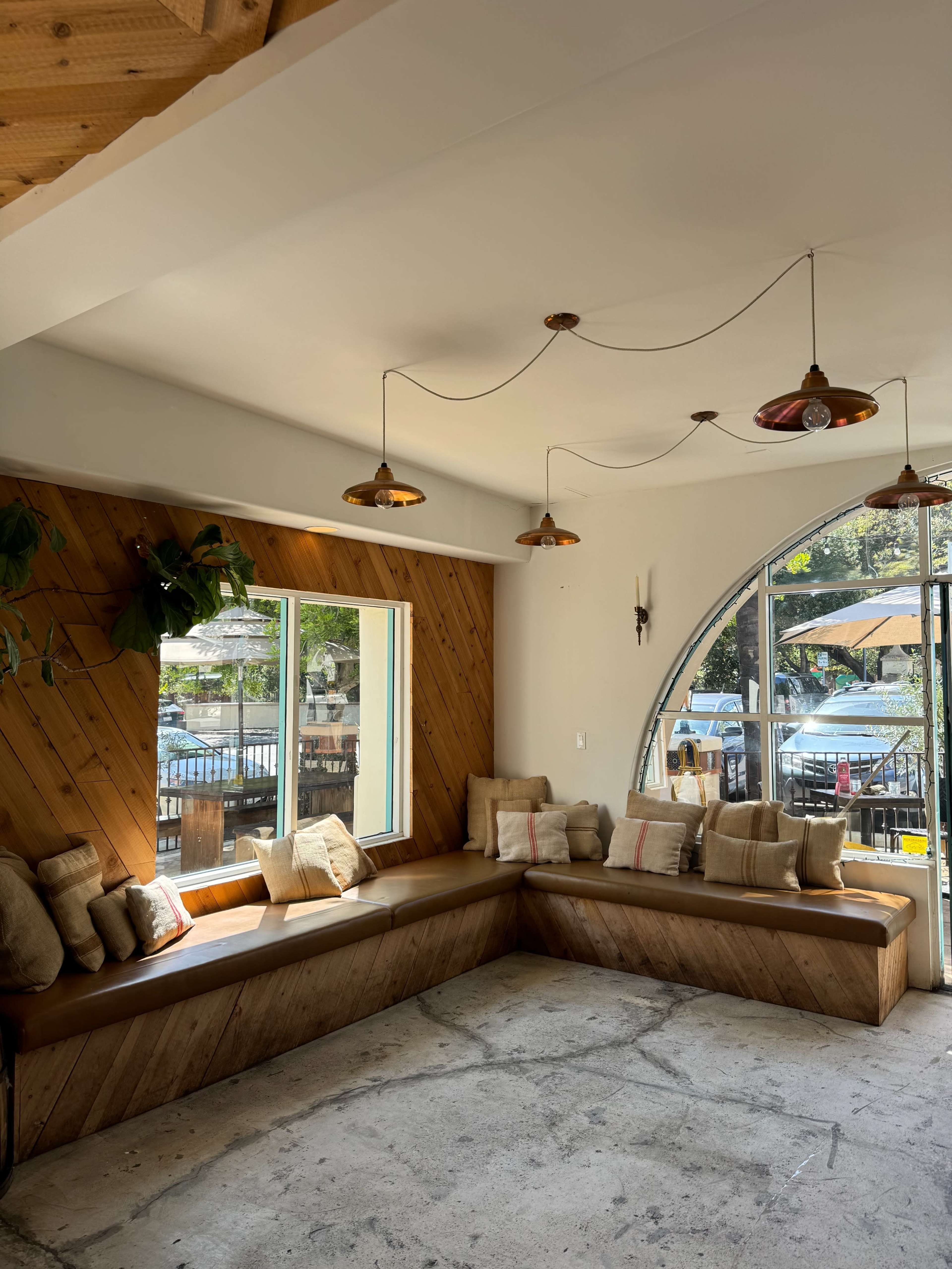 A modern, cozy seating area in a café with a curved window, wooden accents, and pendant lighting.