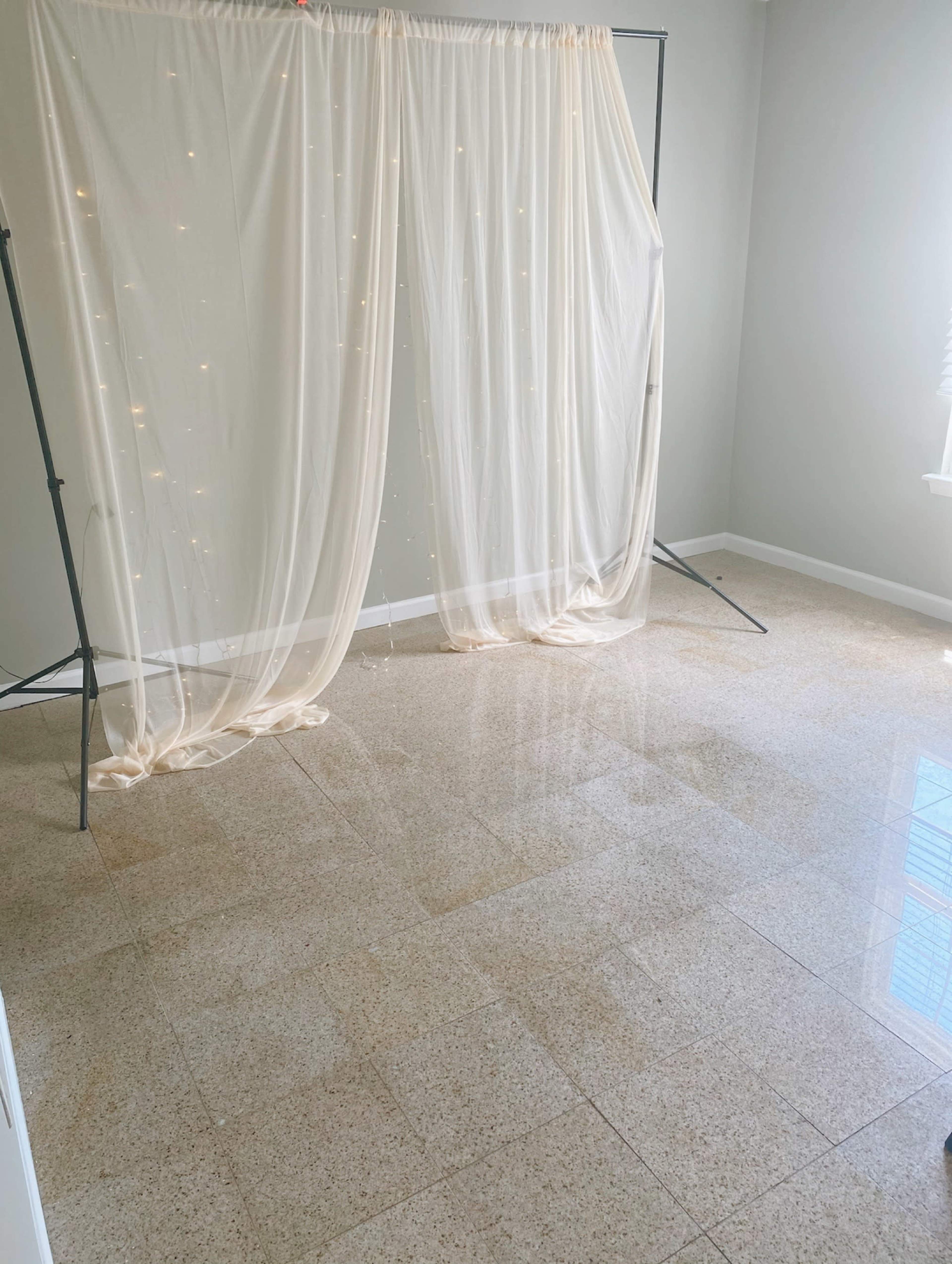 A well-lit room with a glossy tiled floor and a backdrop of sheer fabric draped over a frame, decorated with small lights.