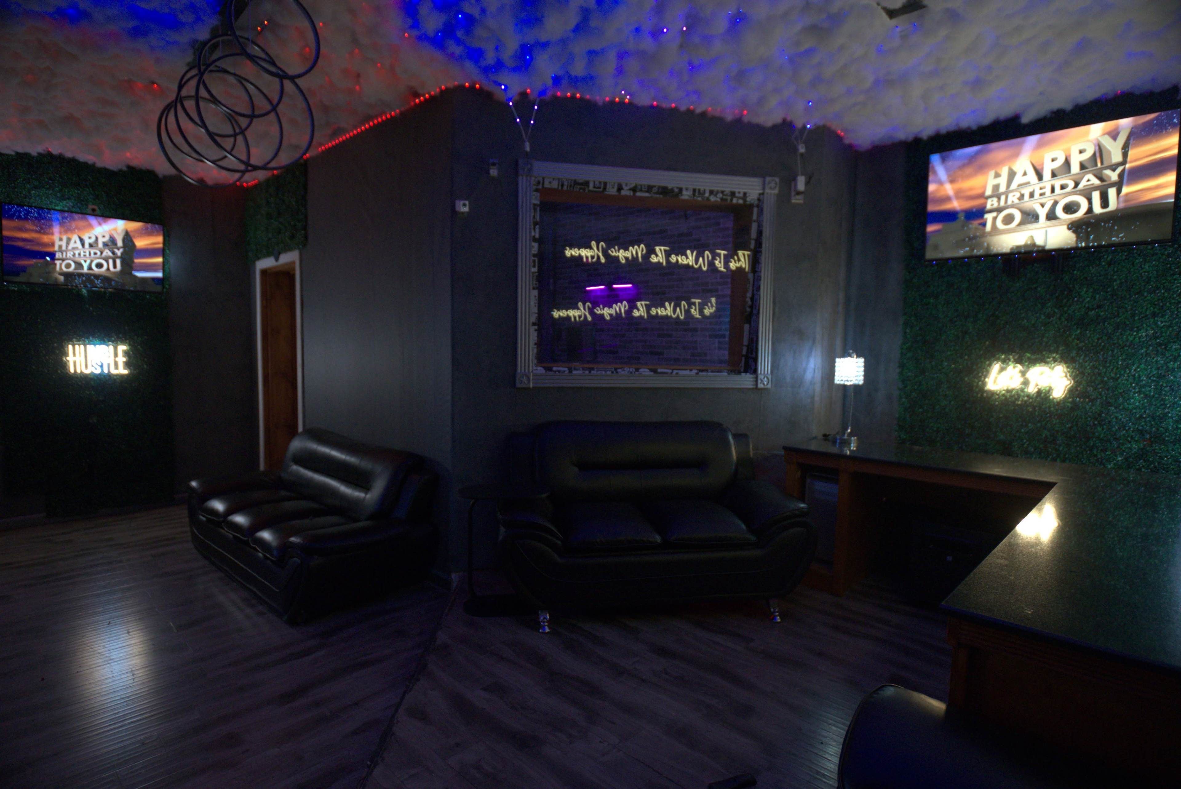 The room features black leather seating, decorative greenery on the walls, and multiple screens displaying birthday messages, illuminated by soft lighting.