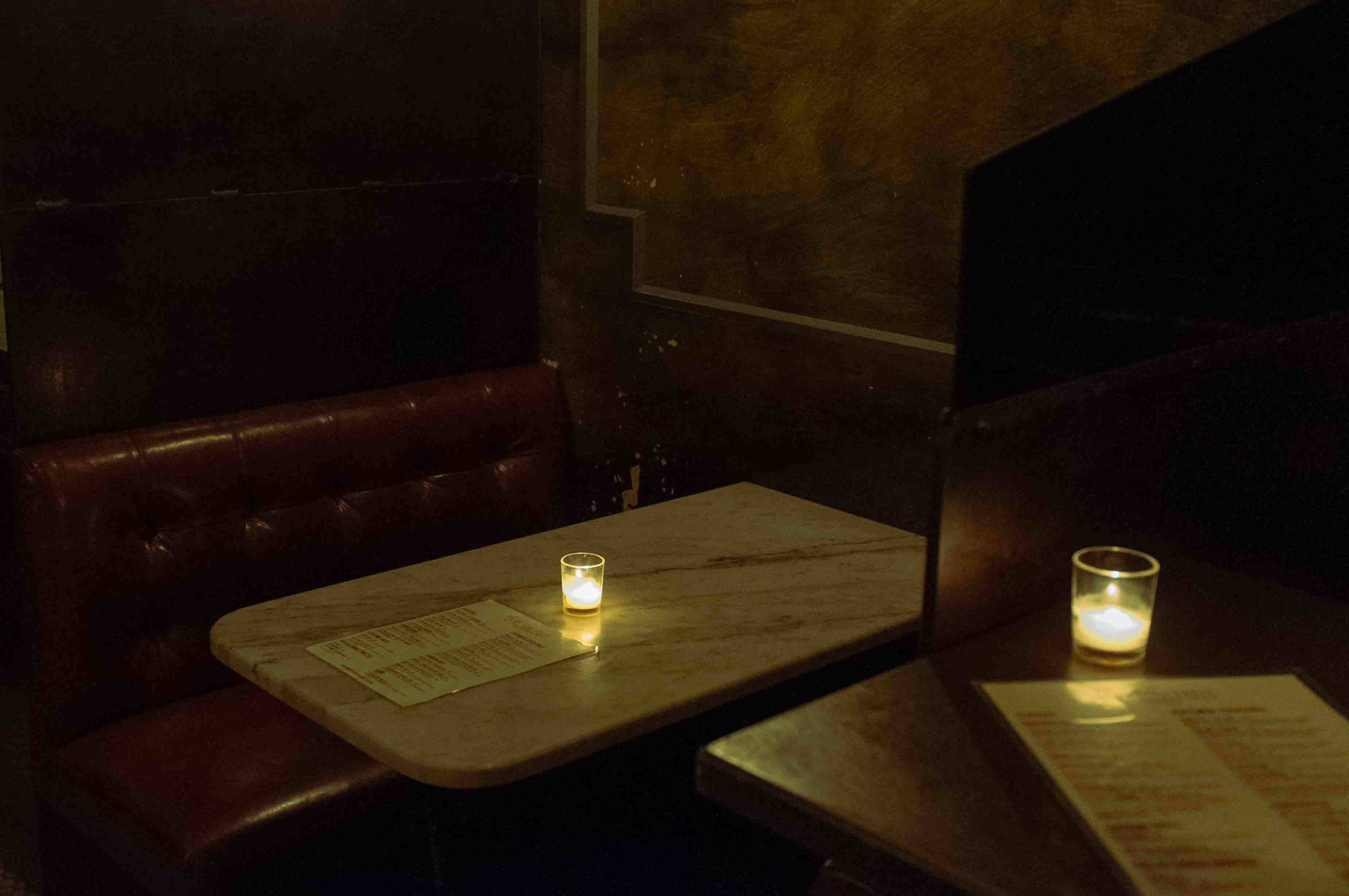 A small, dimly lit booth with a marble table and a candle, accompanied by a menu on a nearby surface.