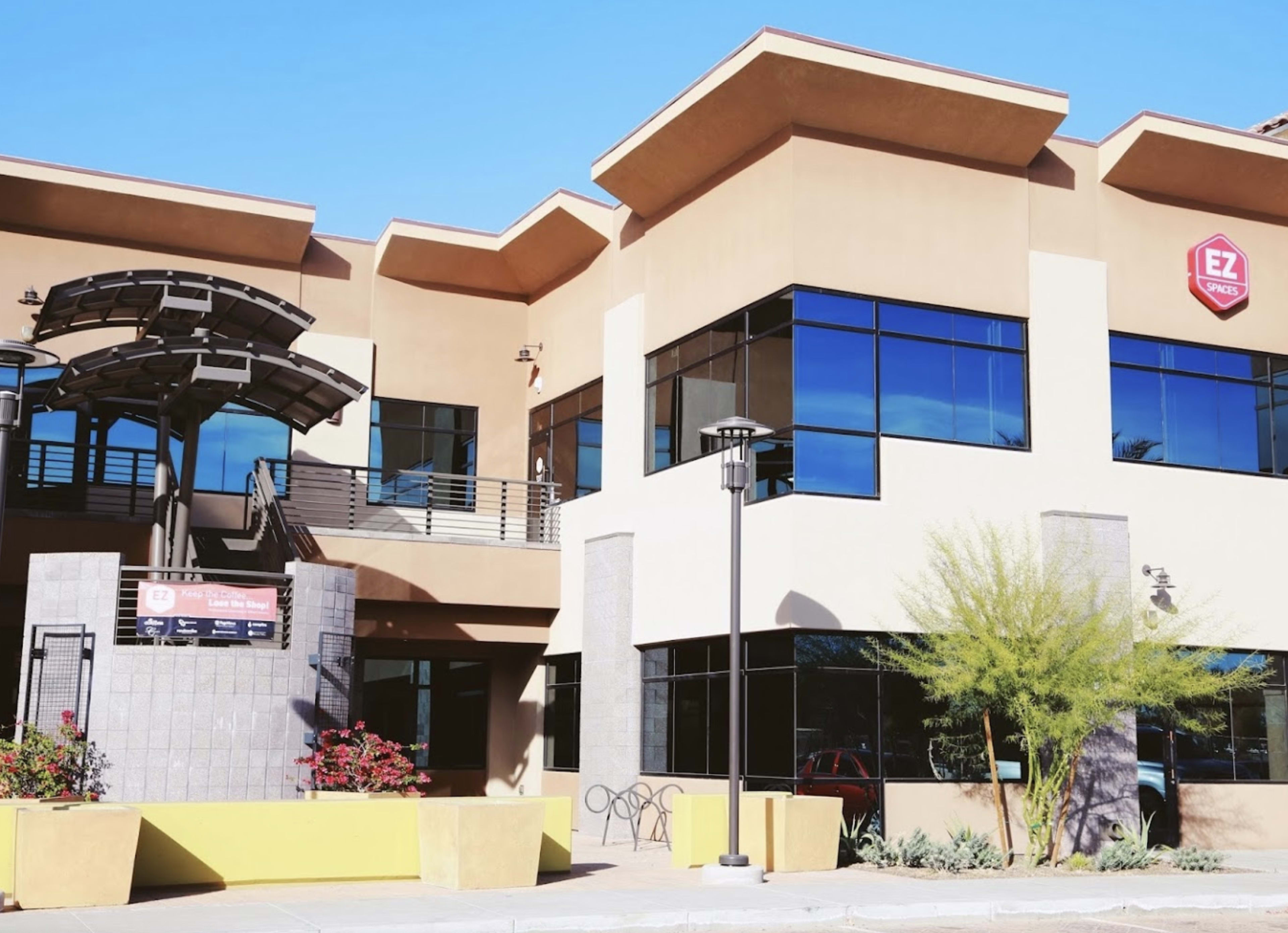 A modern building with large windows, a shaded entrance, and landscaping, along with a sign indicating "EZ" on the facade.