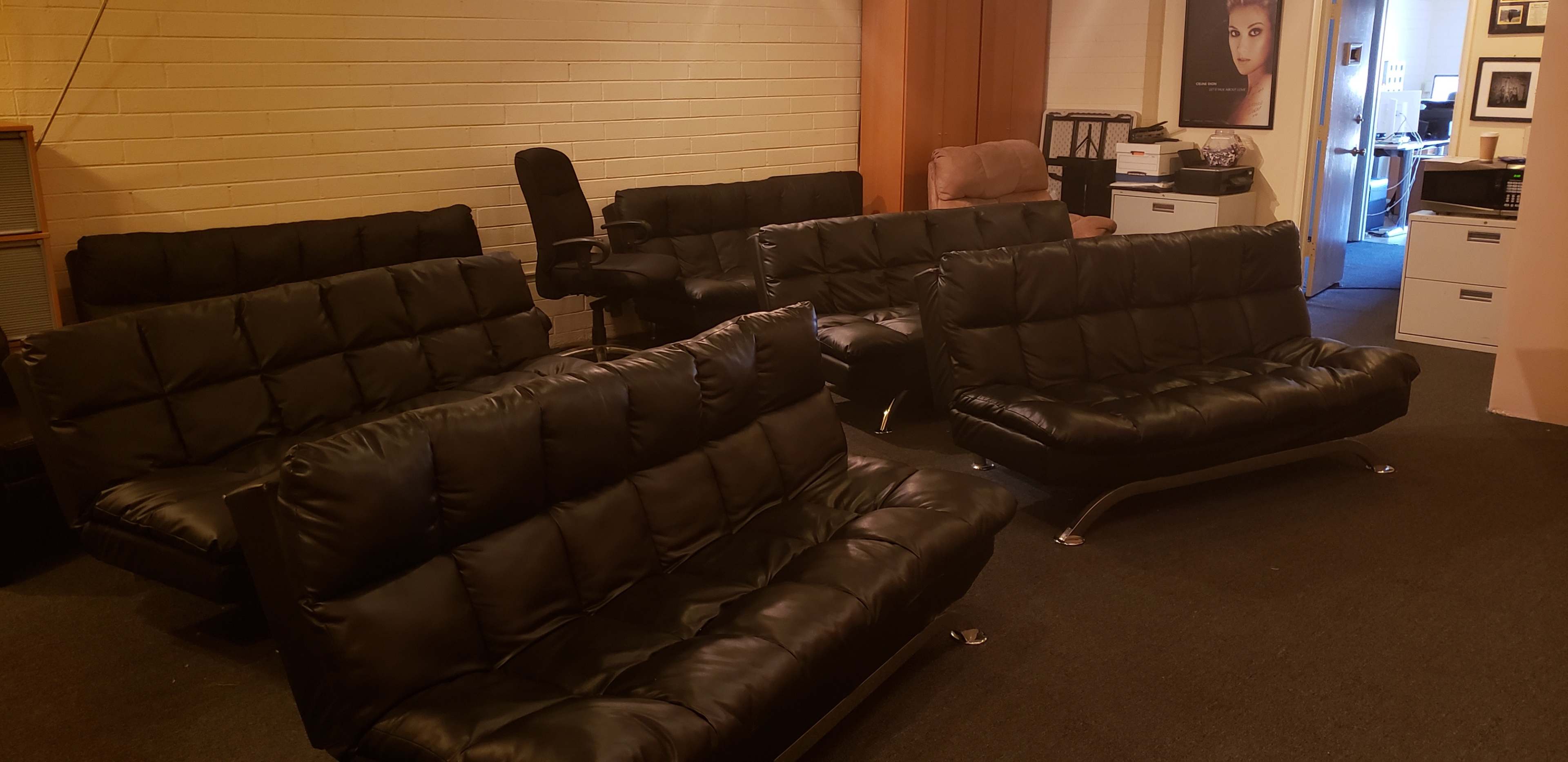 A room with several black leather sofas arranged in a seating area, with a doorway leading to another part of the space in the background.