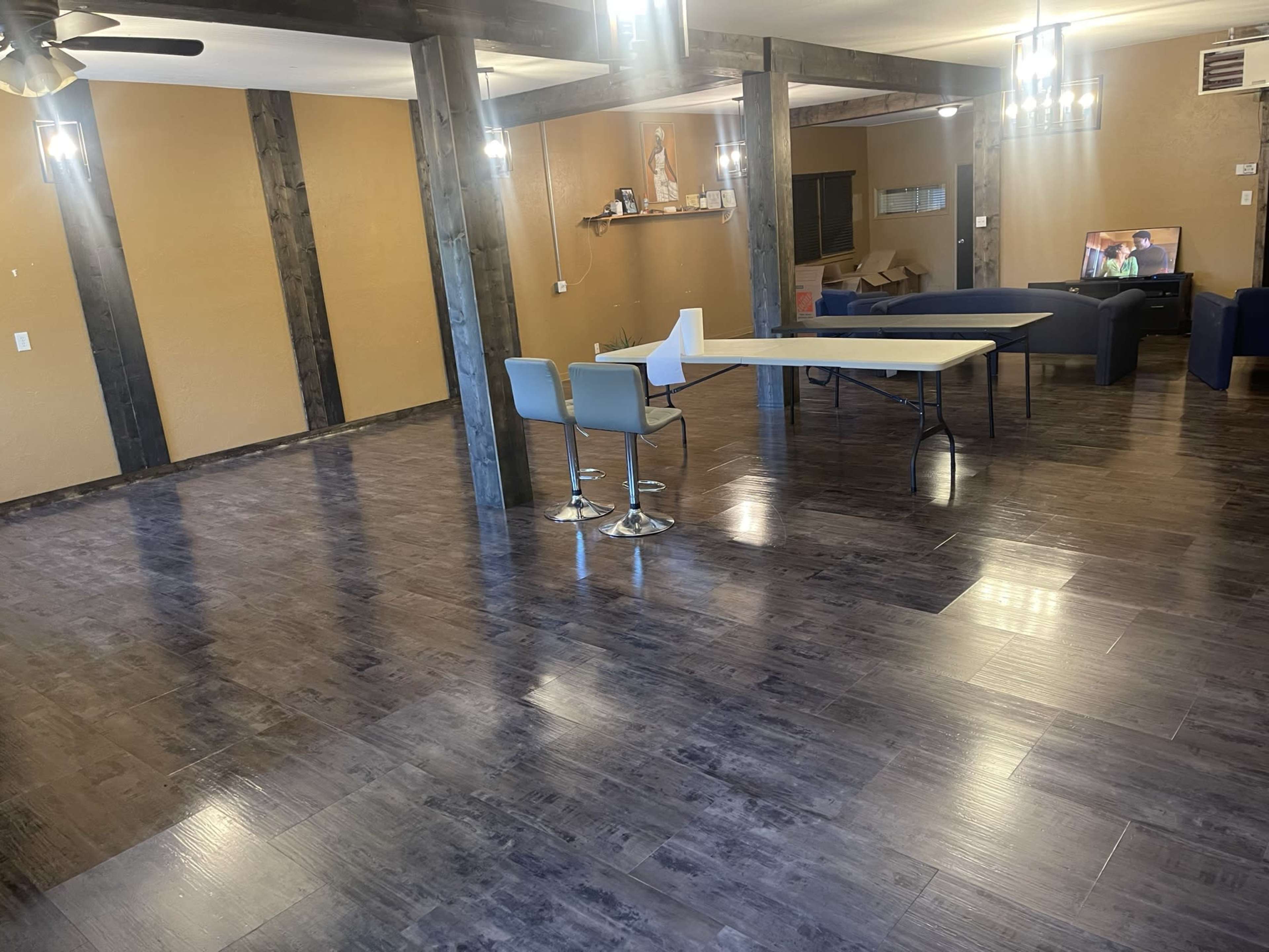 A spacious interior room with wooden beams, dark flooring, a folding table, and a few chairs.